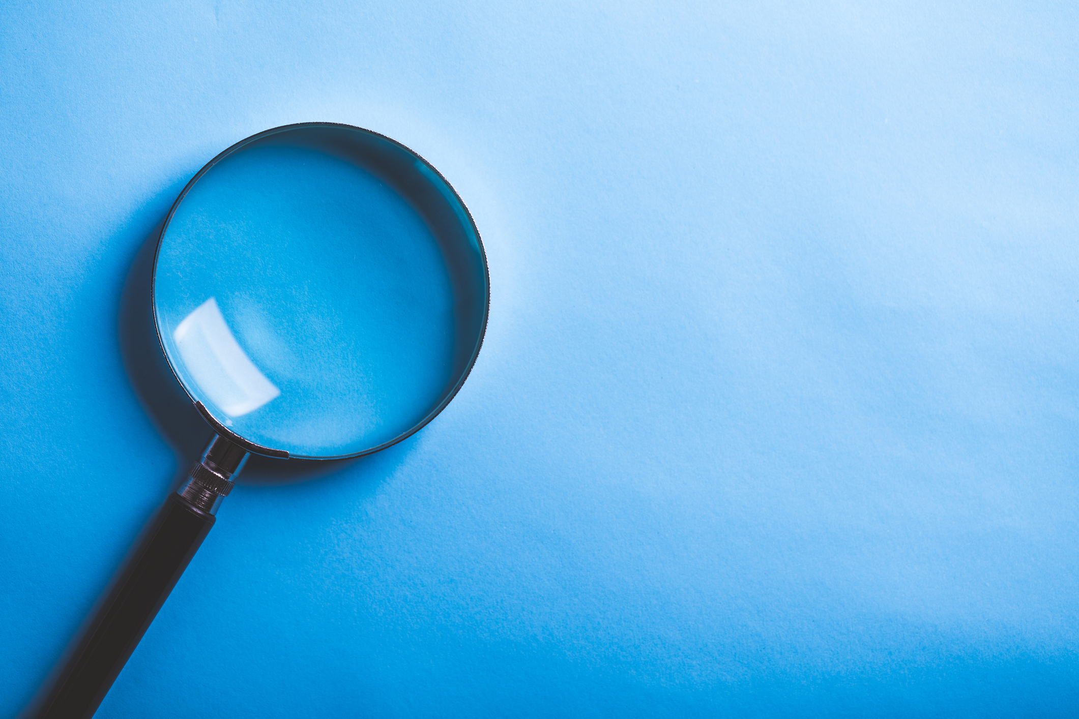 Magnifying glass on the left, on a blue background, light is reflected in the glass