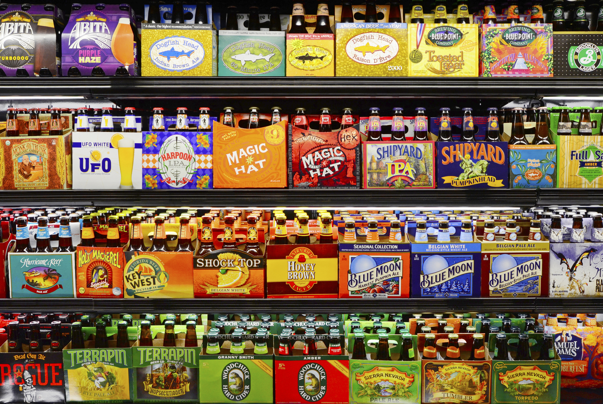Many different kinds of beers sold in six packs in a store, Fort Lauderdale, Florida, four rows in an open refrigerator section, very colorful cardboard on six pack packages
