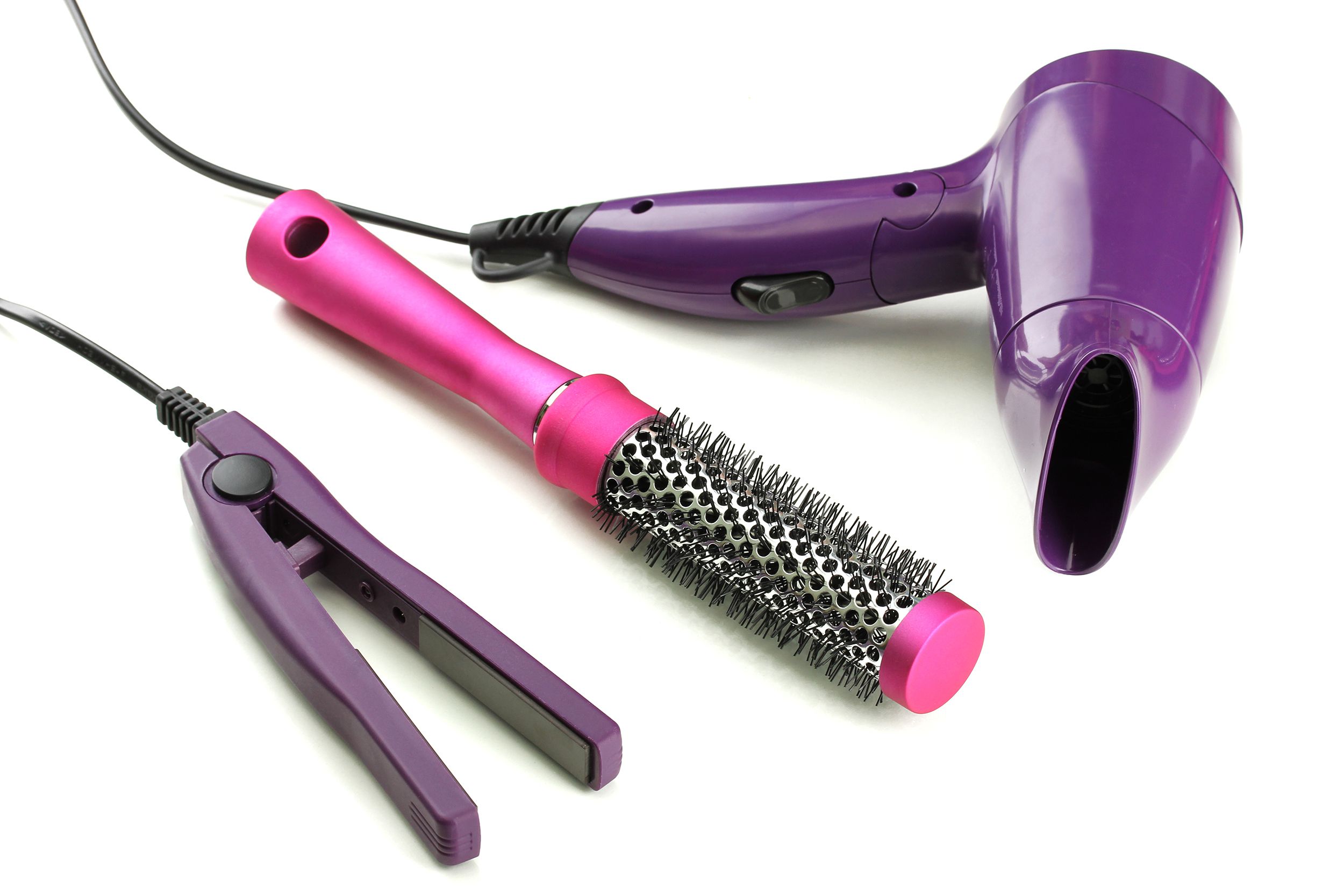 A purple hair straightener, a round pink brush, and a purple hair dryer, on a white background