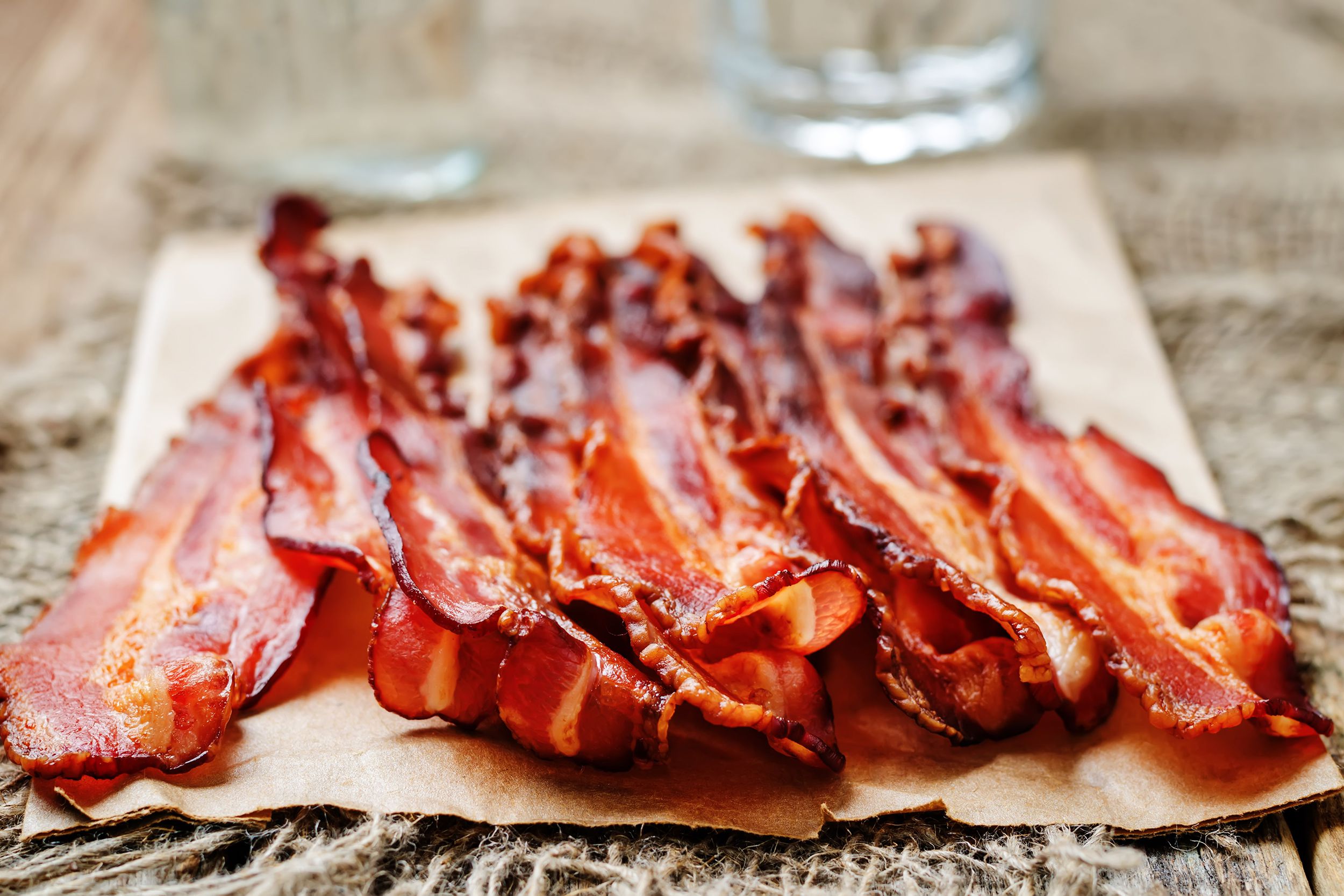 Several pieces of cooked bacon, selective focus to the foreground bottom, on a brown paper bag, blurred background, top