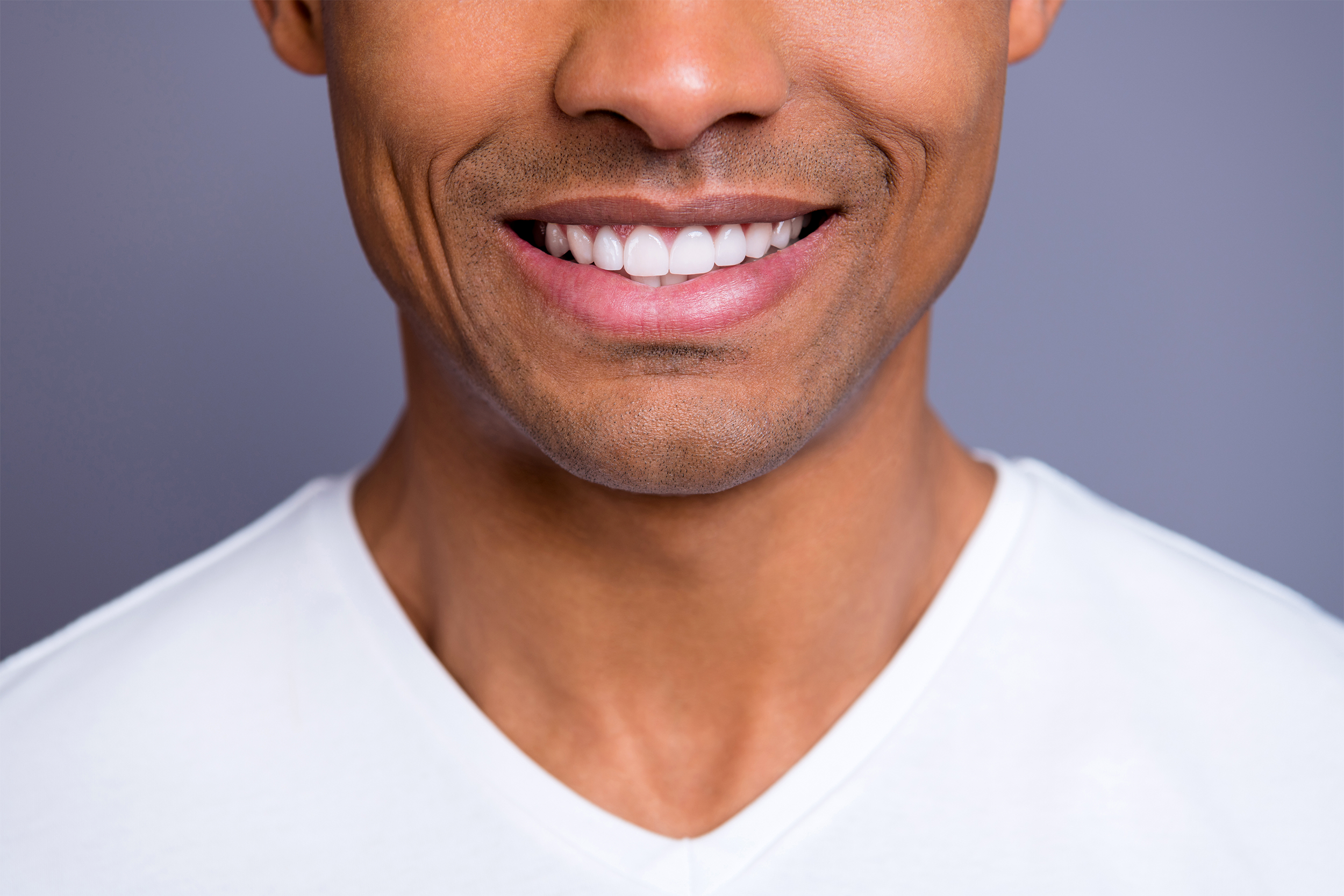 Smile of a young man, cropped lower face and upper body, wearing a white t-shirt, on a dark grey background