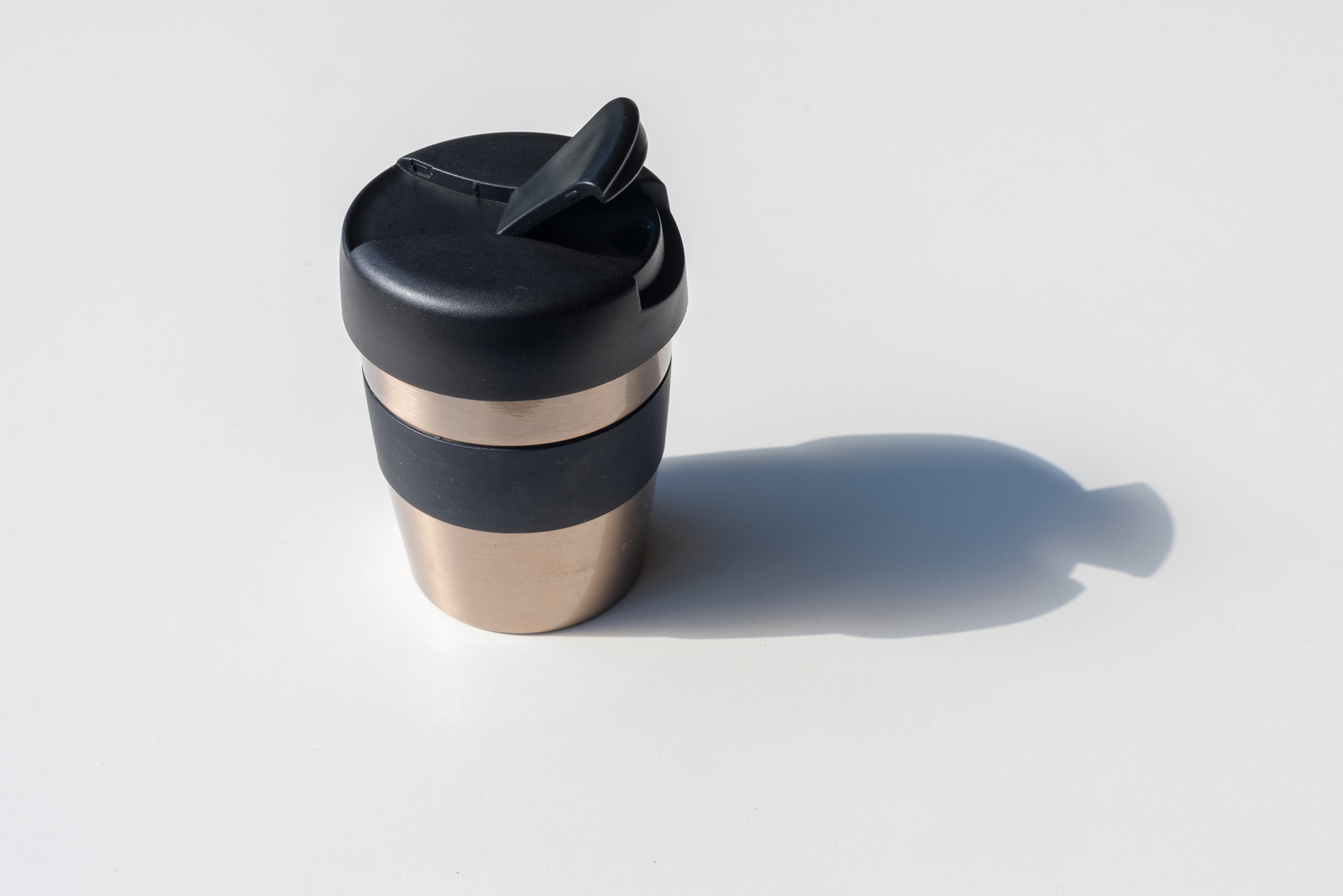 Stainless steel thermos mug with lid, shadow of it to the right, on a light grey background