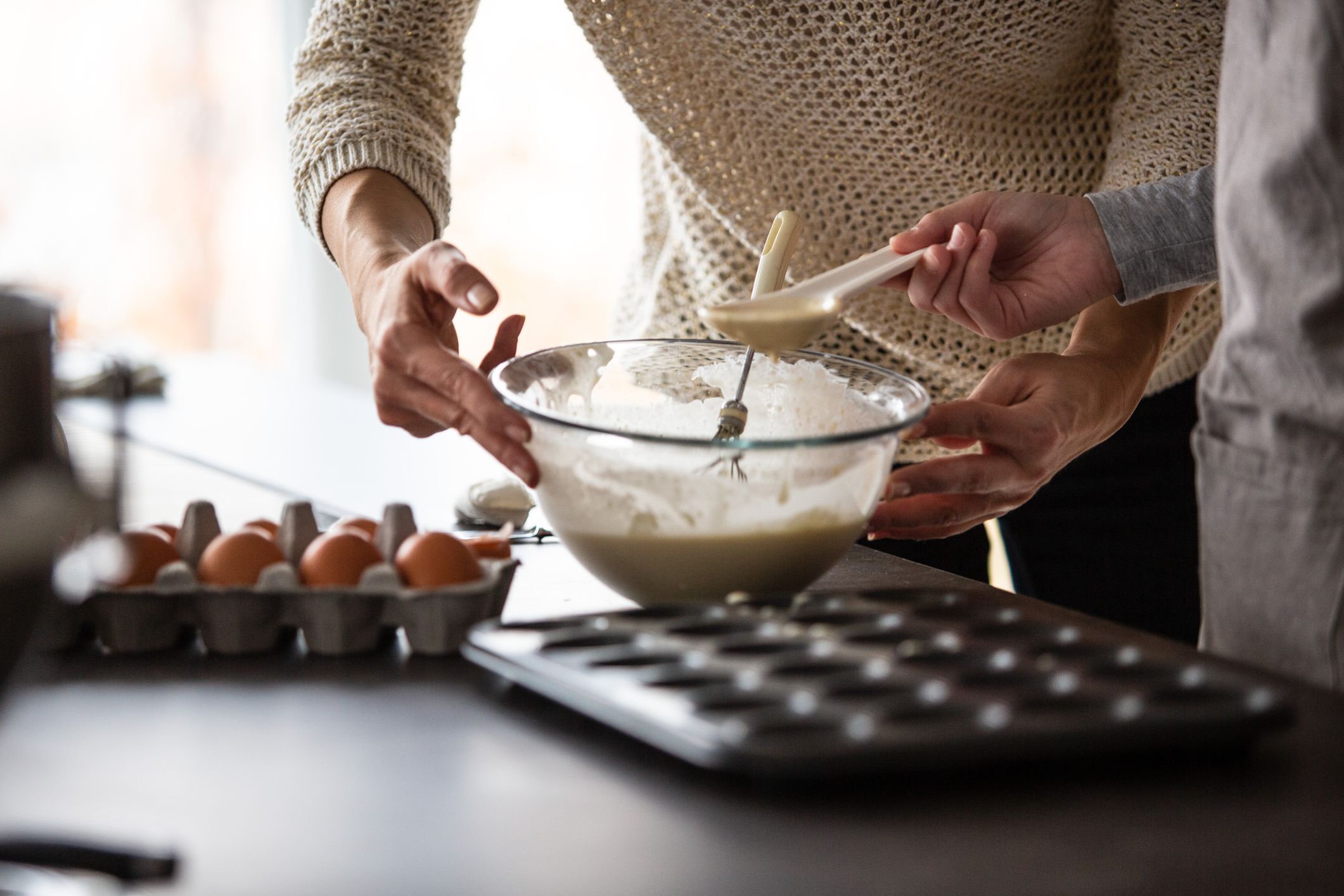 Close-up shot of mid adult woman and her daughter scooping batter into muffin tin at the kitchen counter.