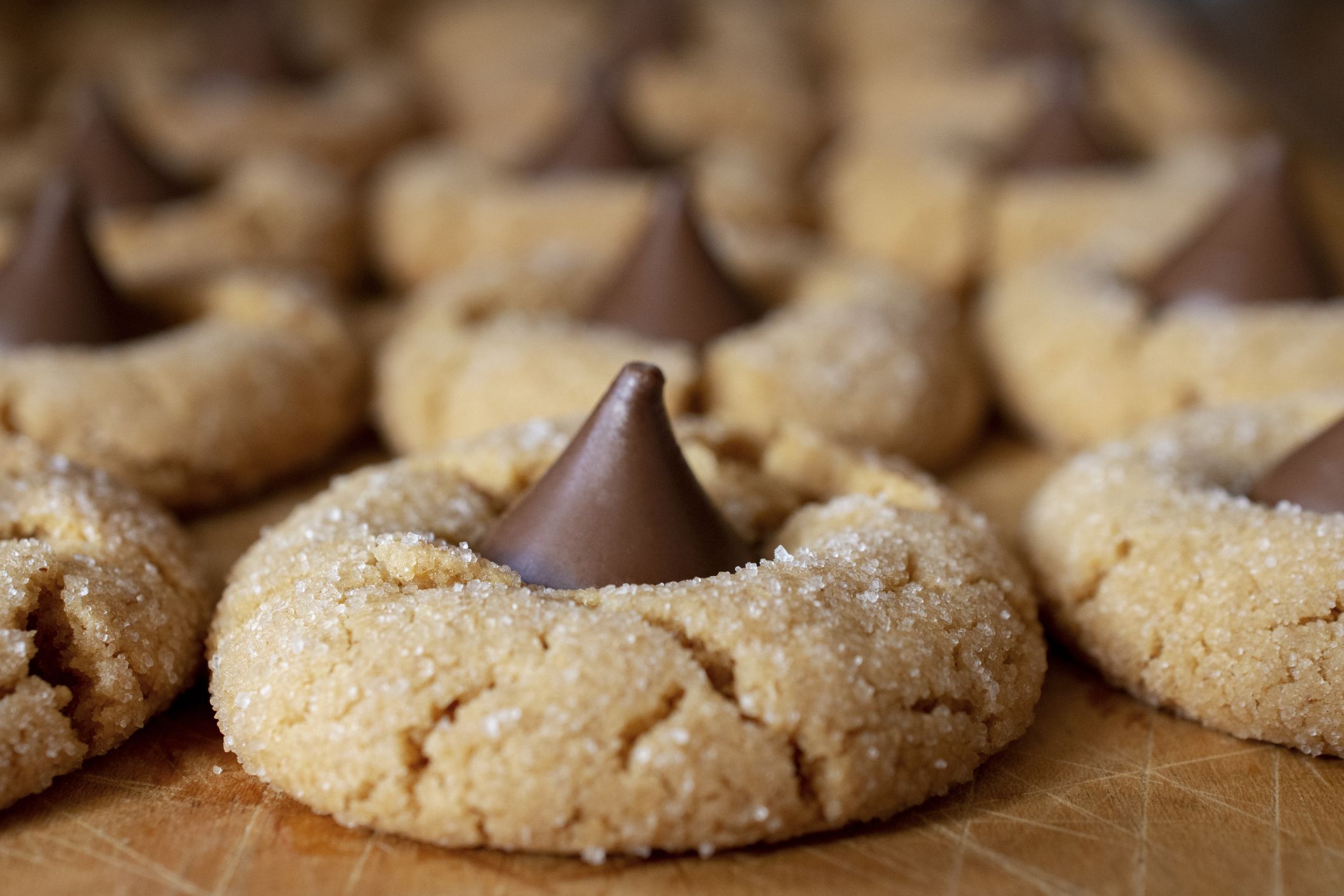 Peanut butter blossom cookies up close with rows of cookies behind on wooden cutting board. Macro shot.