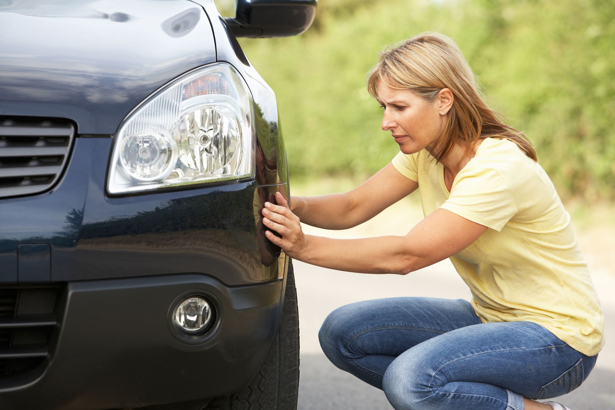 Female Driver Broken Down On Country Road Checking Wheel of Car