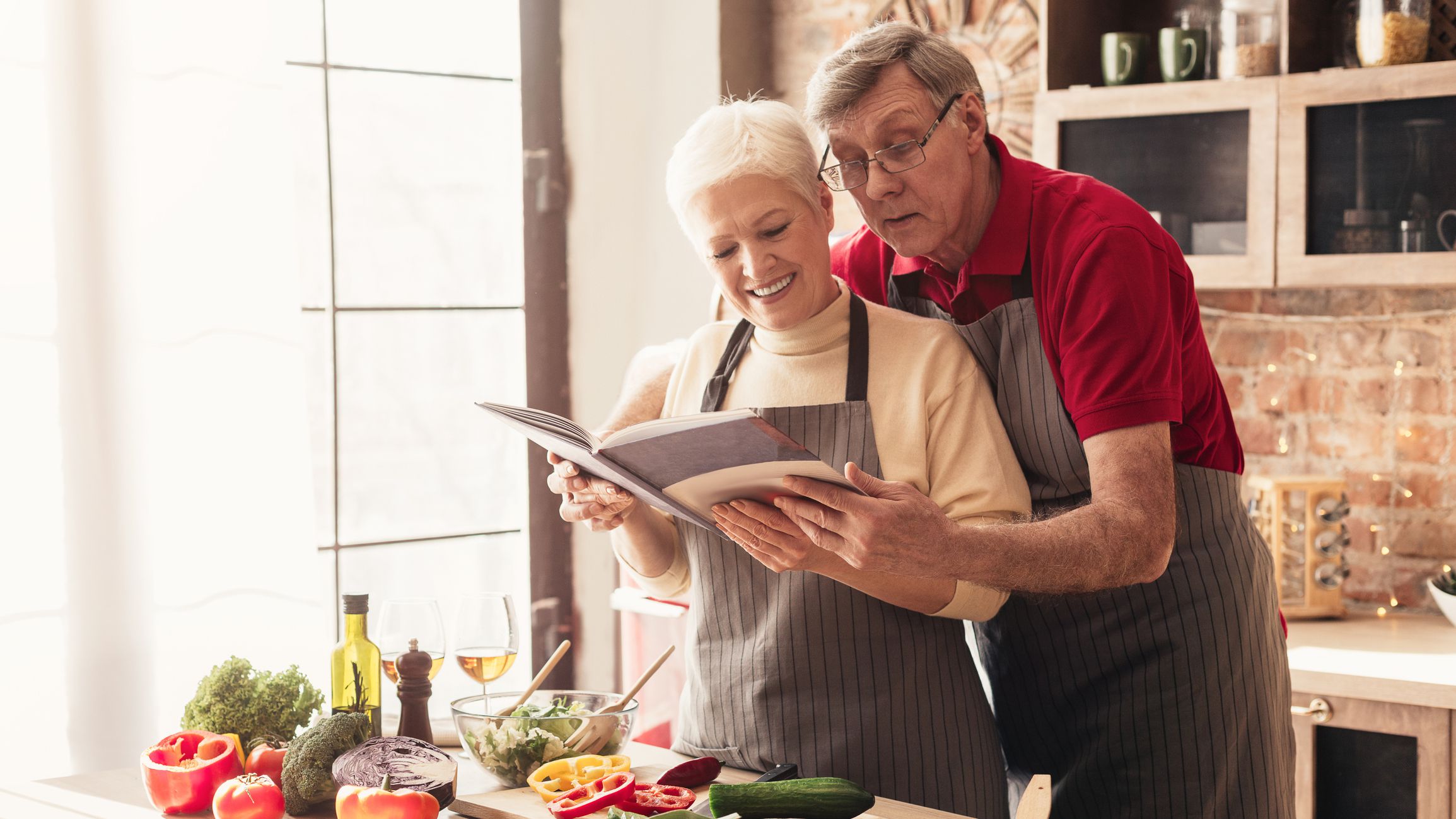 Family cookbook. Senior couple reading recipes at kitchen interior, panorama, empty space