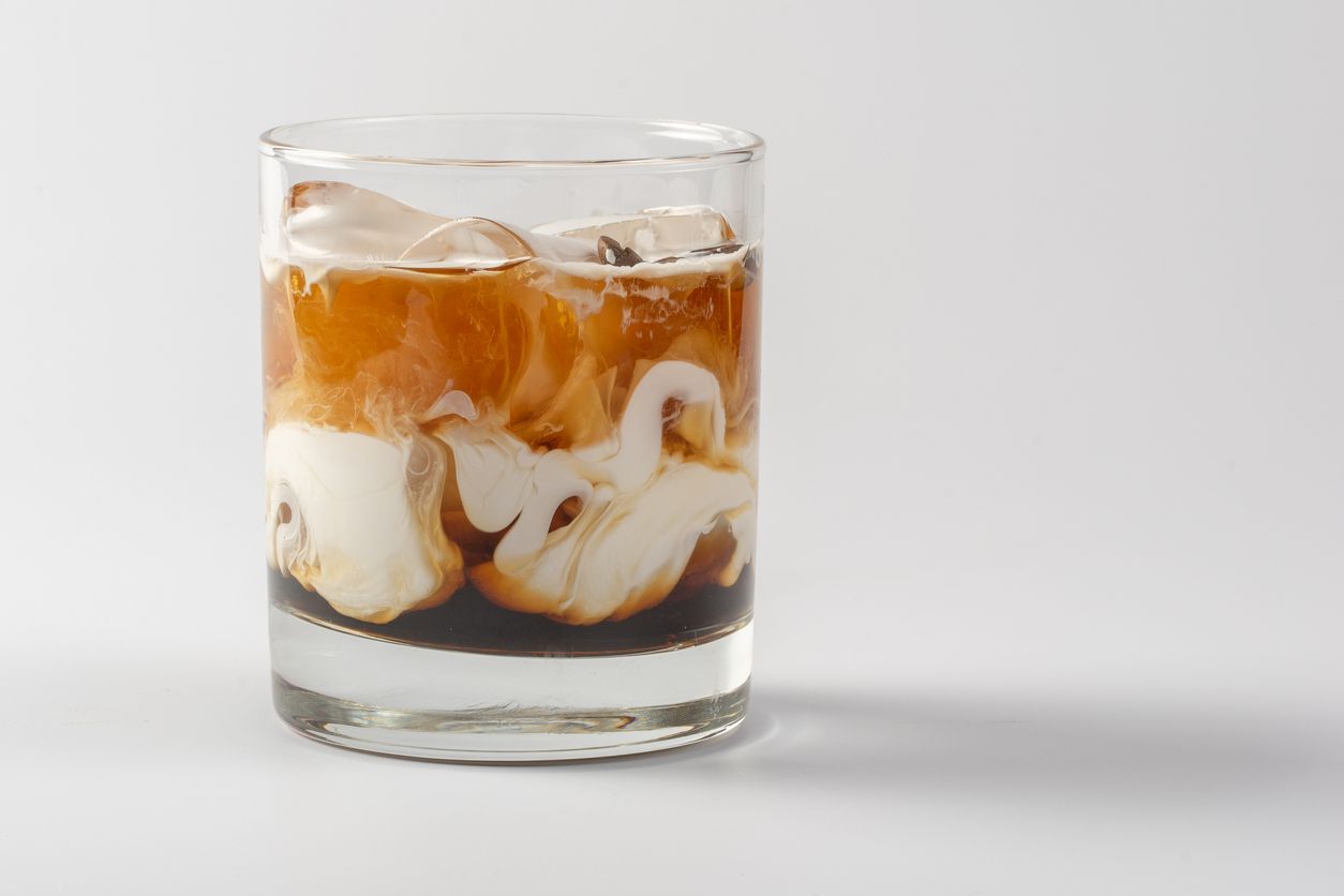 A glass of coffee with cream in it.