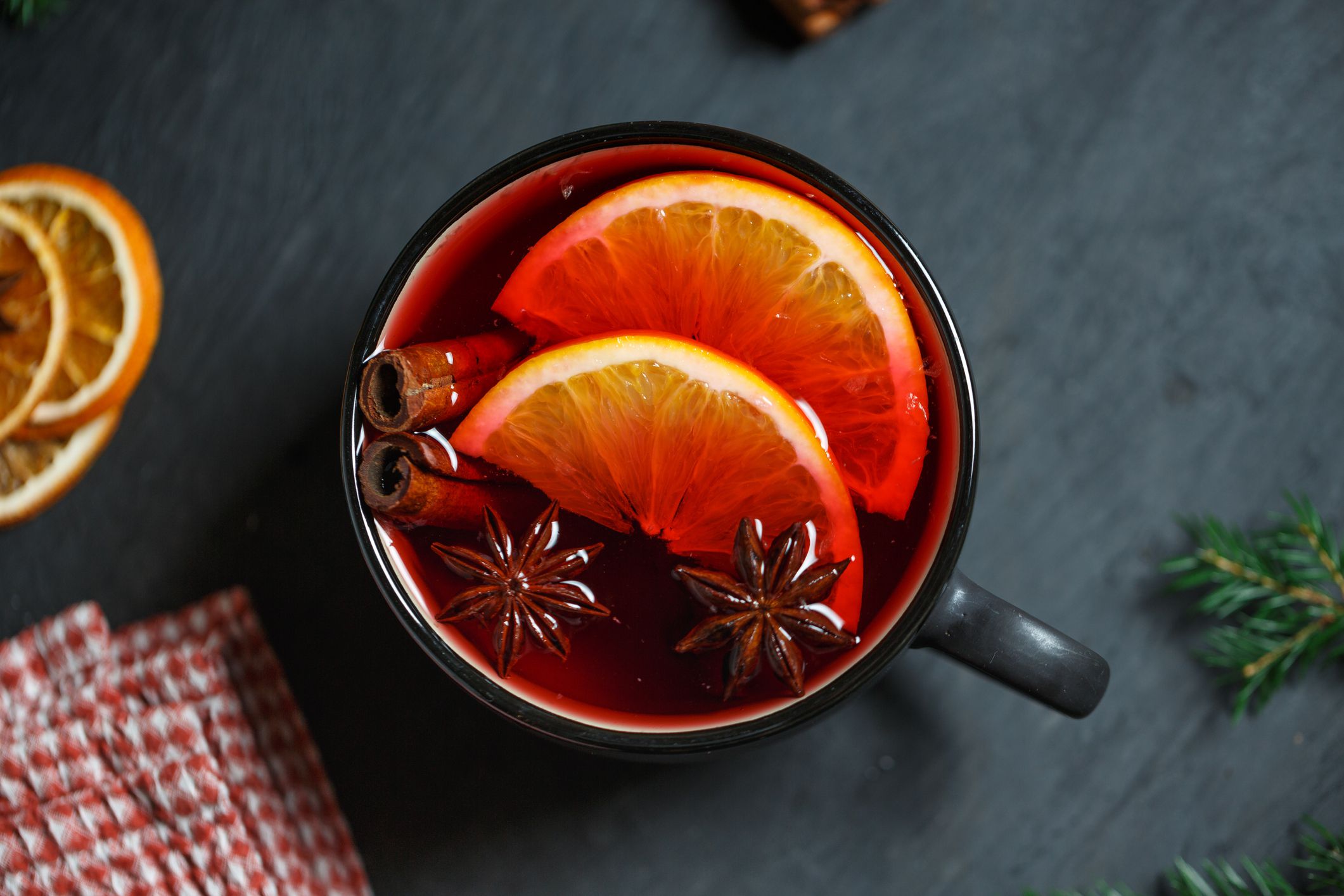 Black mug with bright red mulled wine, two slices of orange, cinnamon and star anise on a dark gray table