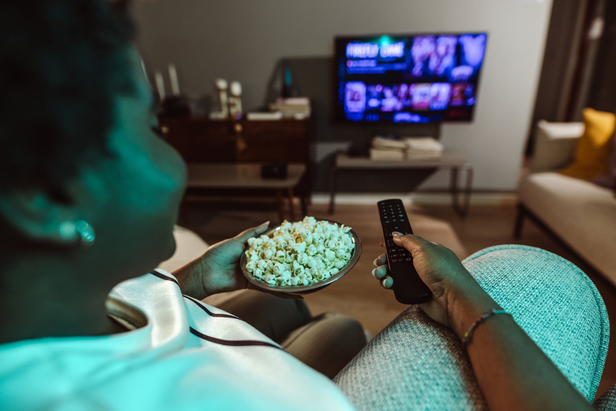 Cheerful smiling woman is watching TV and holding the remote control. Cozy night at home