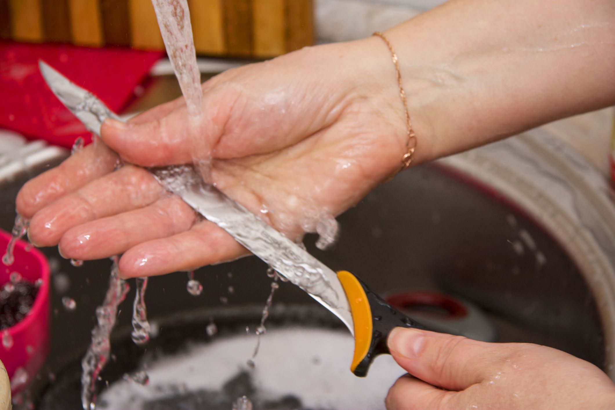 Woman washing the long knife by hands in the sink in the kitchen under clean running water