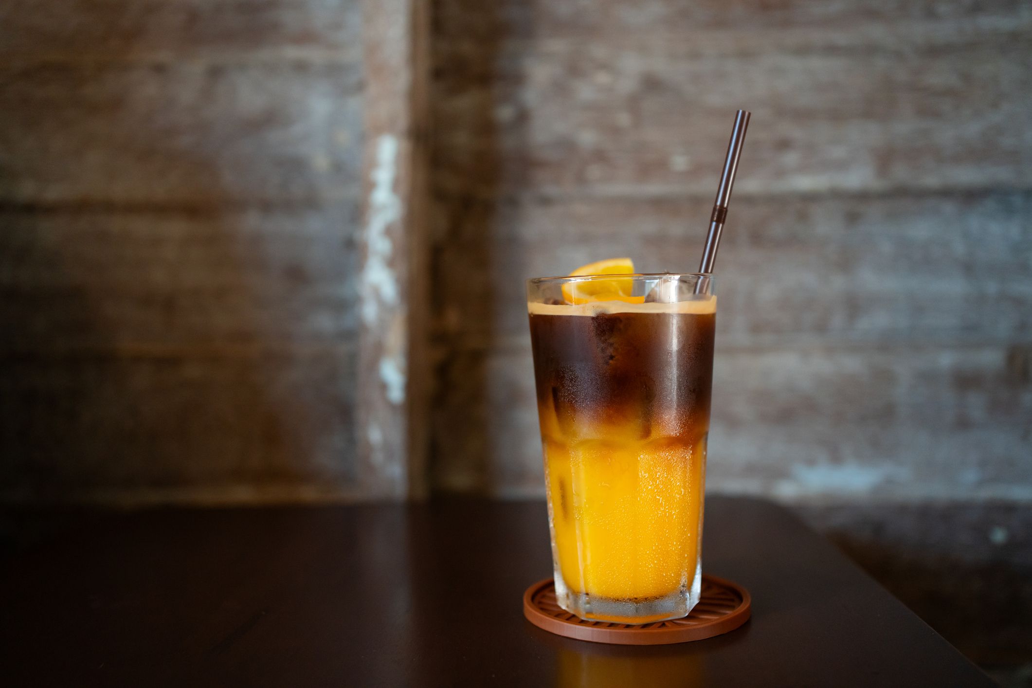 Iced Americano mixed with orange juice in a glass, placed on table with wooden wall background.