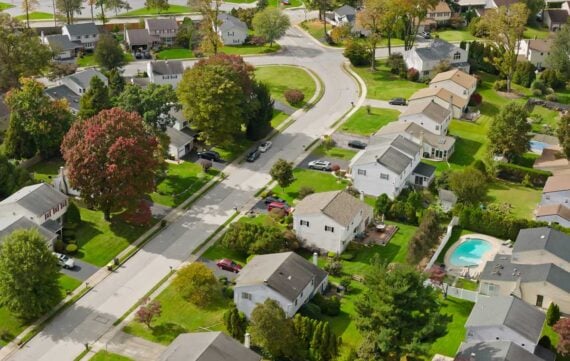 Aerial view of a suburban neighborhood with tree-lined streets, single-family homes, green lawns, and a backyard swimming pool&mdash;an ideal setting to compare property tax rates by state in this quiet residential area.