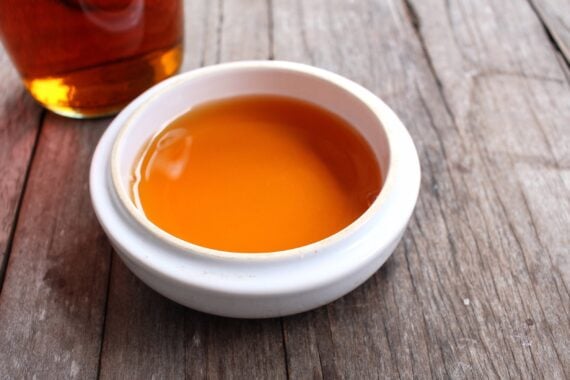 A small white bowl filled with amber-colored liquid, sitting on a rustic wooden surface.