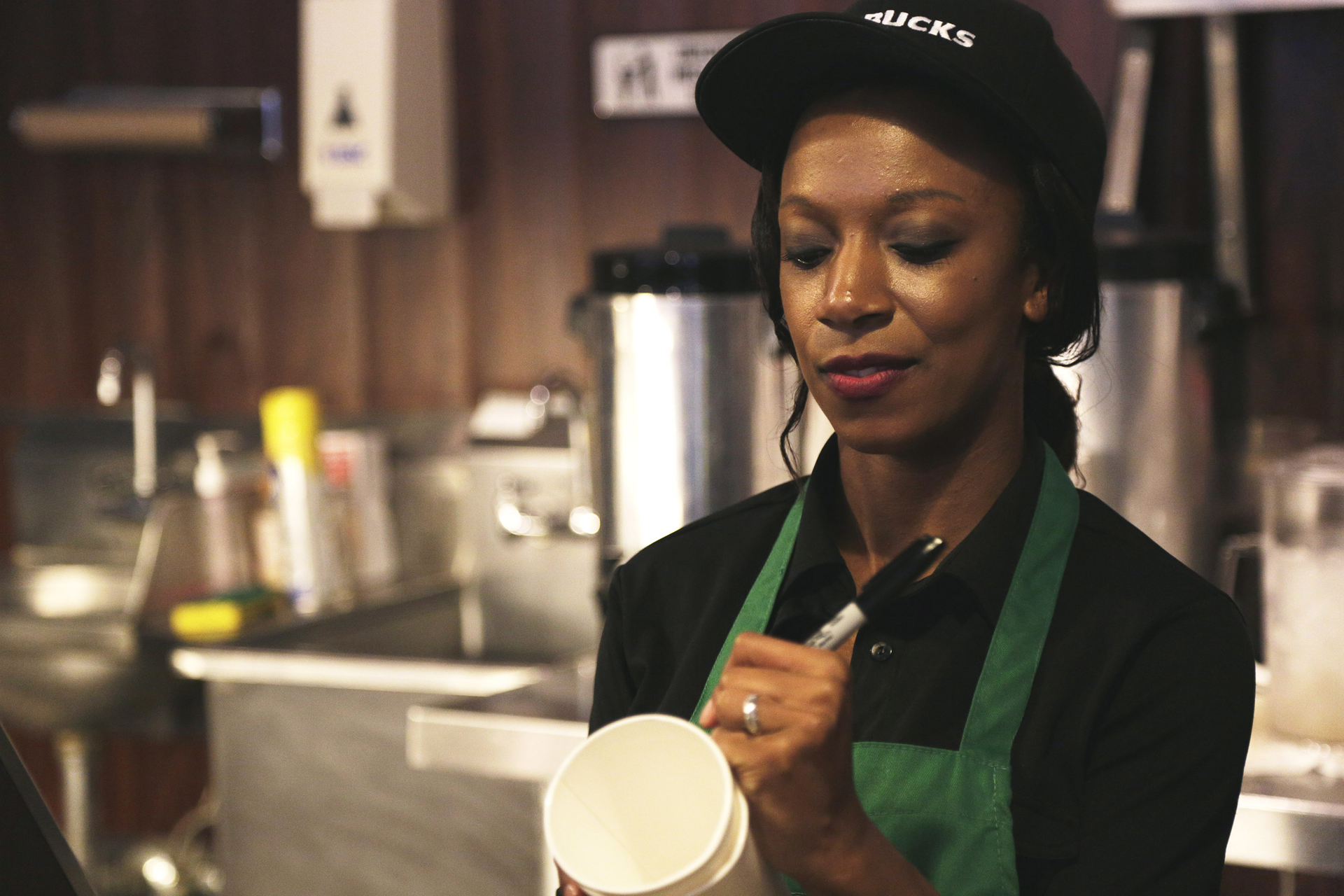 Female Starbucks Cashier With a Slight Smirk, Preparing a Cup for a Starbucks Drink