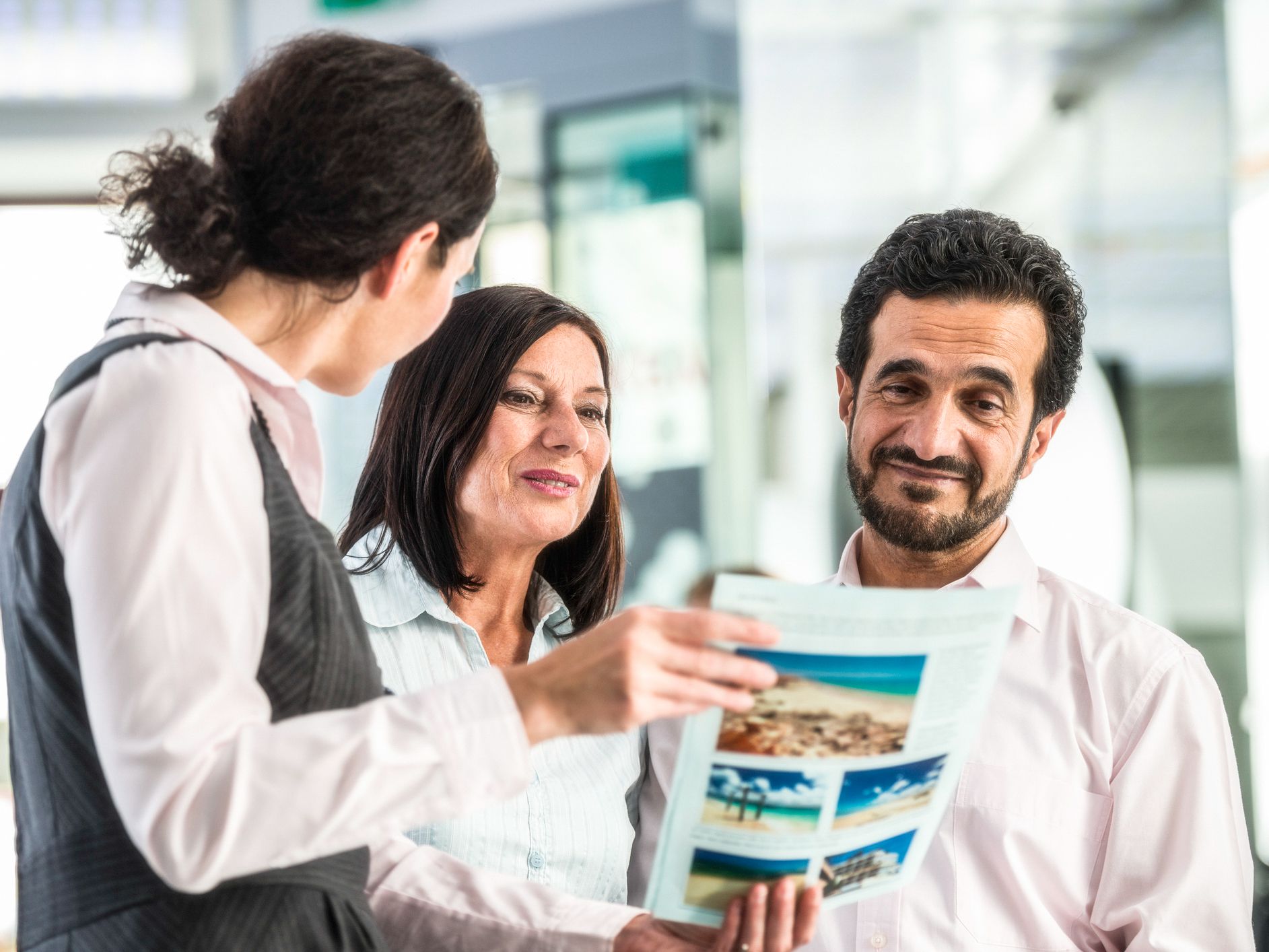 Female travel sales agent explaining the offer from a holiday flyer to a senior couple in the travel agency.