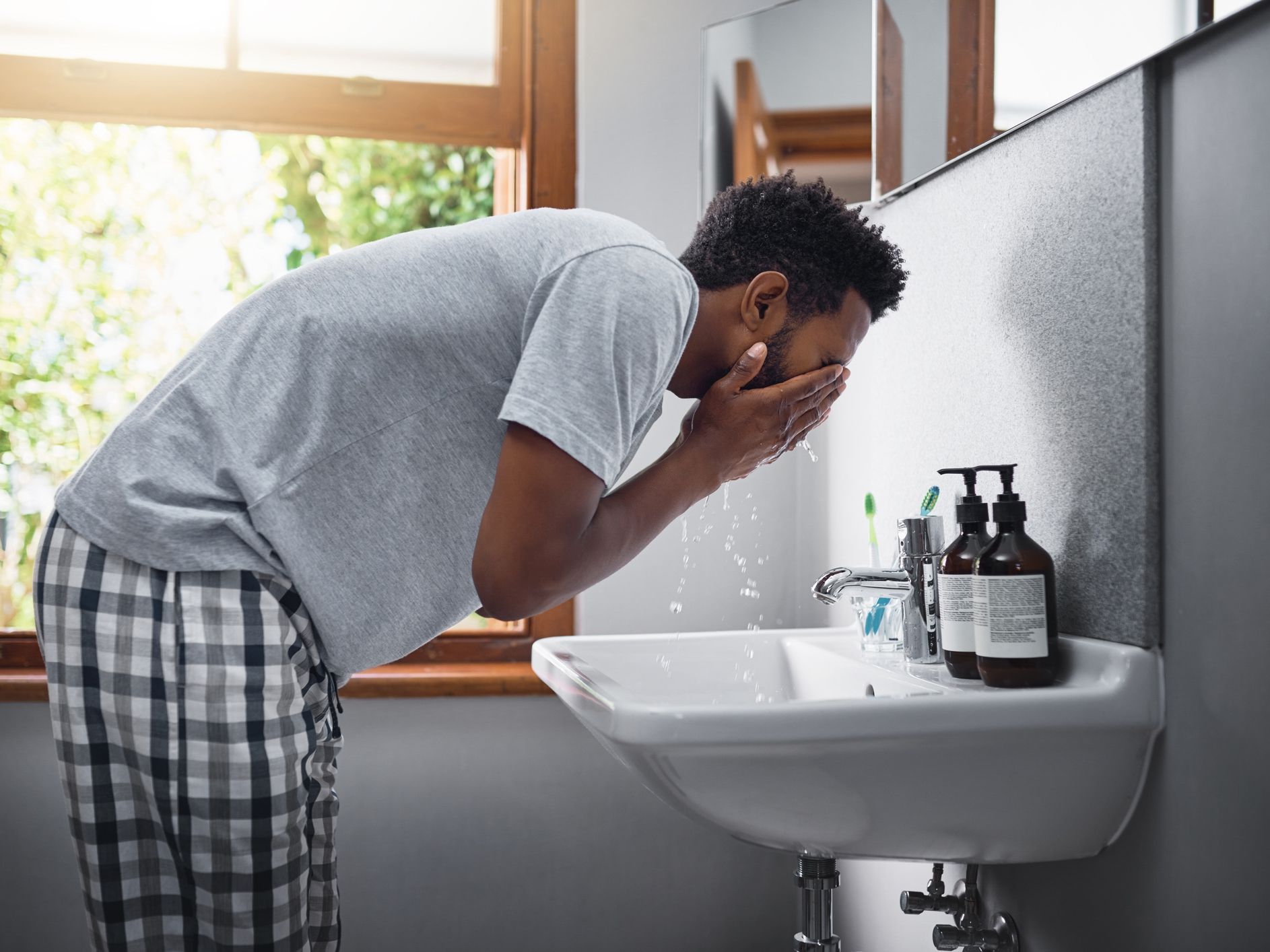 Cropped shot of a handsome young man washing his face in the bathroom at home