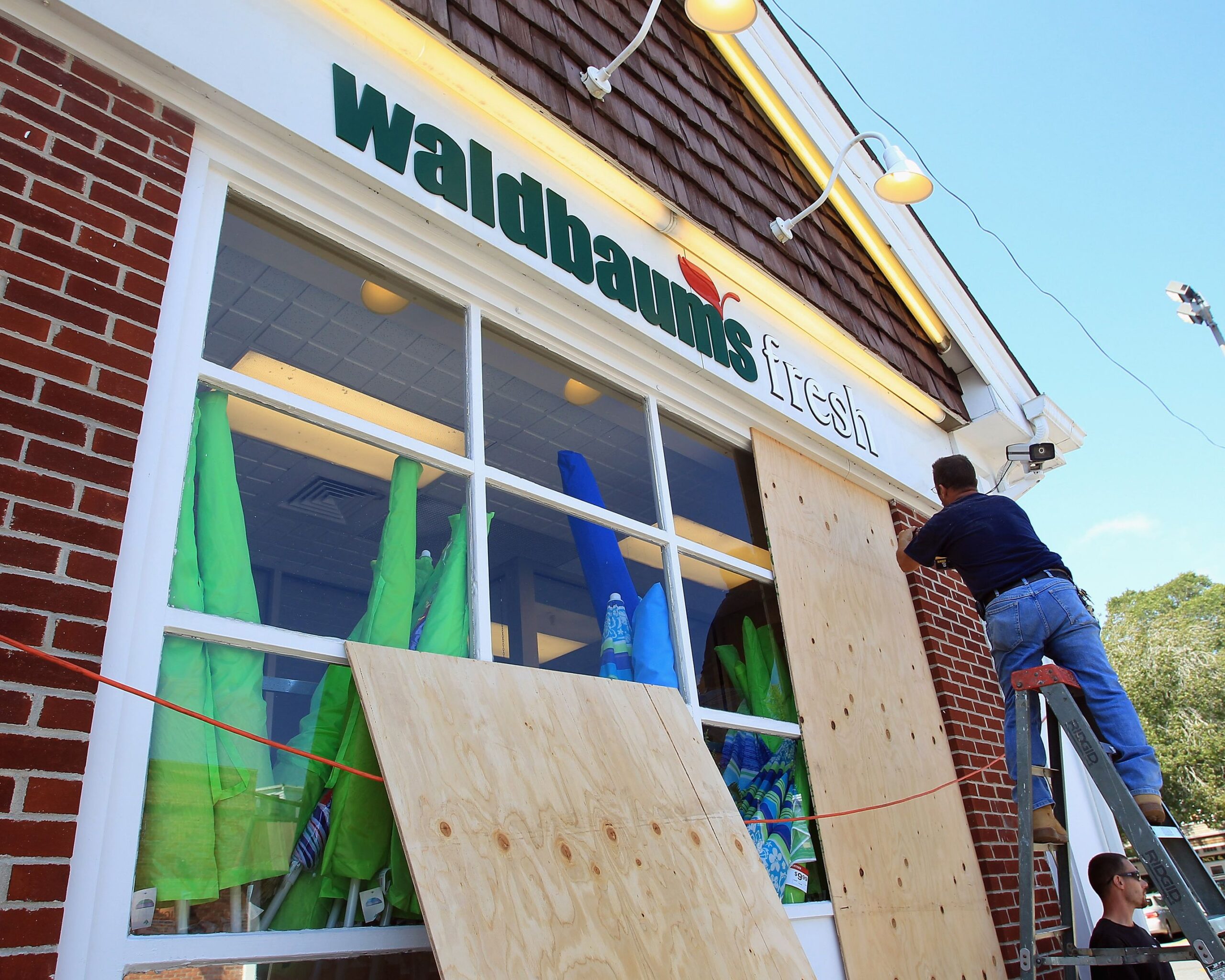 Exterior windows of Waldbaum's Grocery Store, East Hampton, New York, man is putting up boarding in preparation for Hurricane Irene, red brick building, on a sunny day