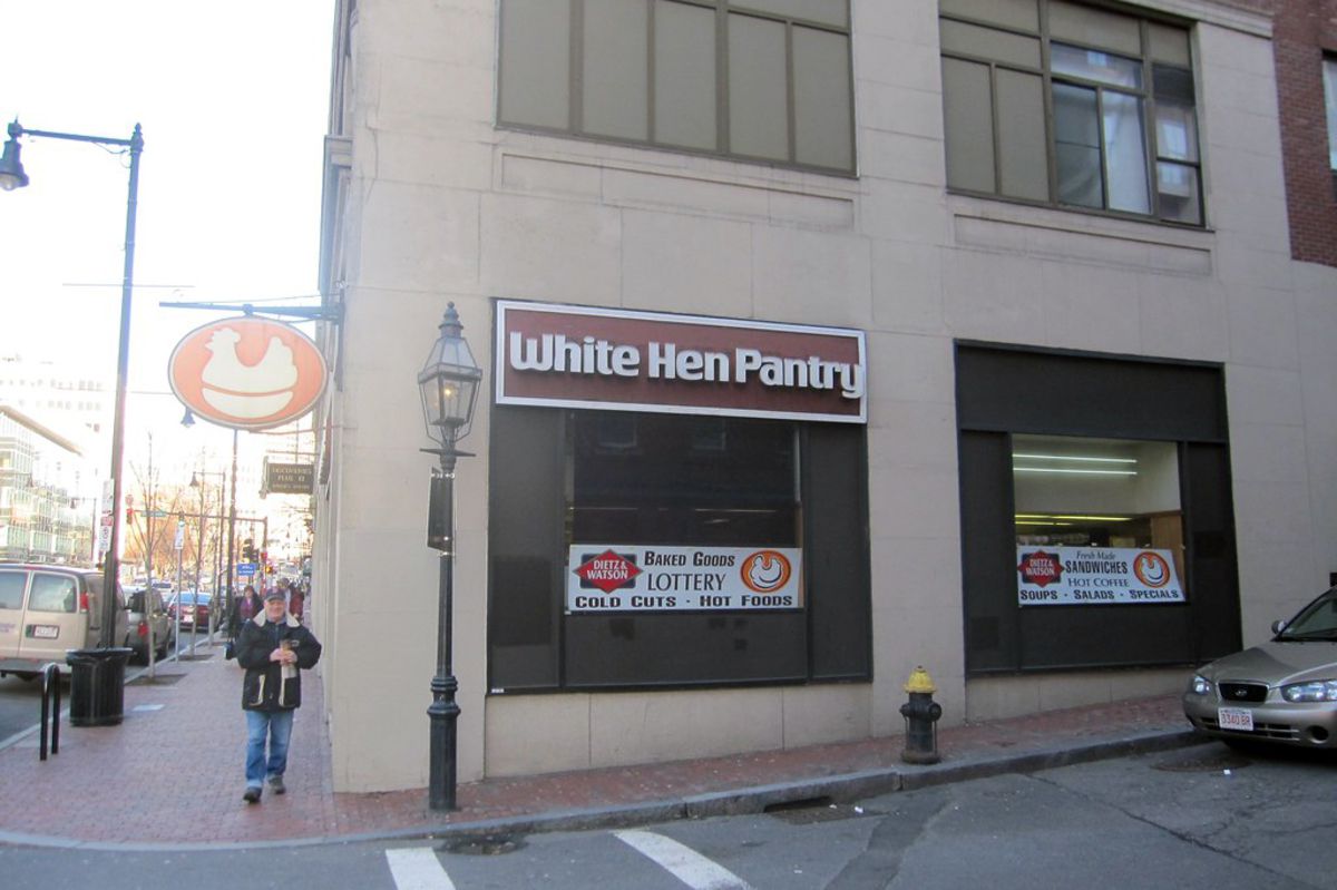Side exterior of White Hen Pantry, Boston, on a street corner, beige building with brick sidewalk, street in the foreground, on a sunny day during winter