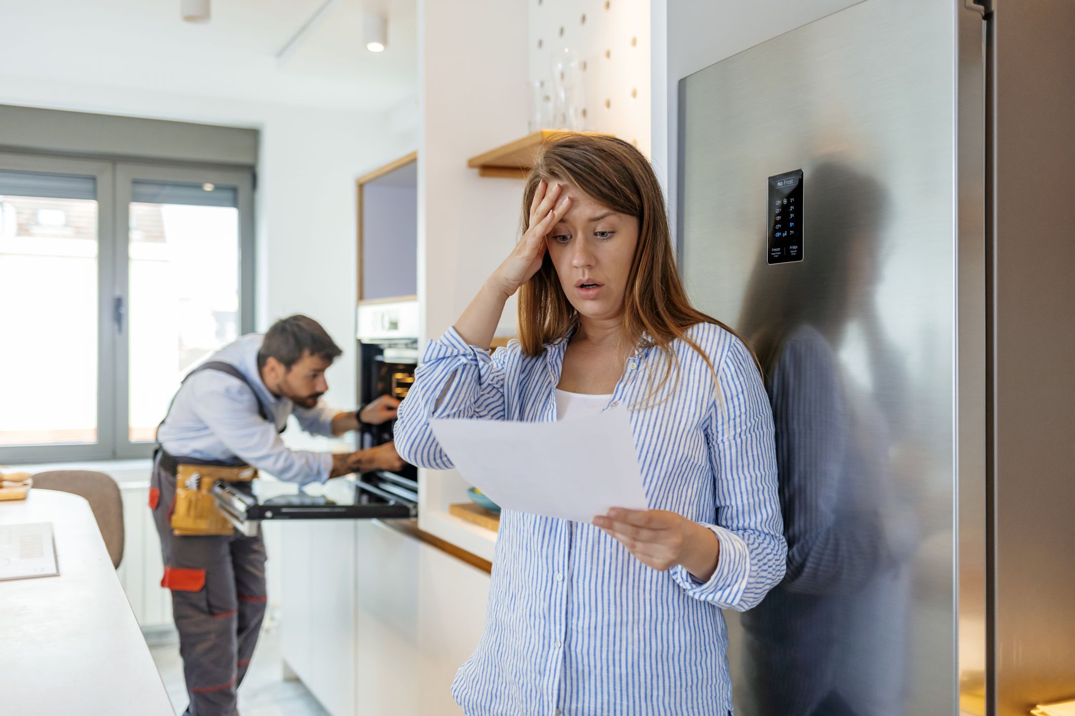 Young Frustrated Woman Looking At Huge Bill From Plumber Standing In Kitchen