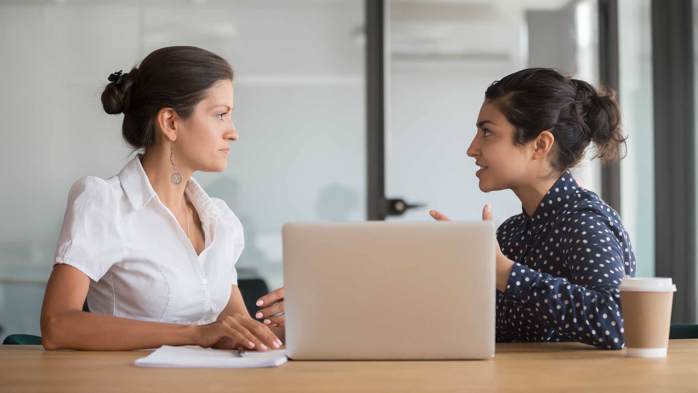 Enthusiastic young indian employee sharing new project ideas with serious female boss. Diverse business woman team discussing working moments at office. HR manager listening to interns experience