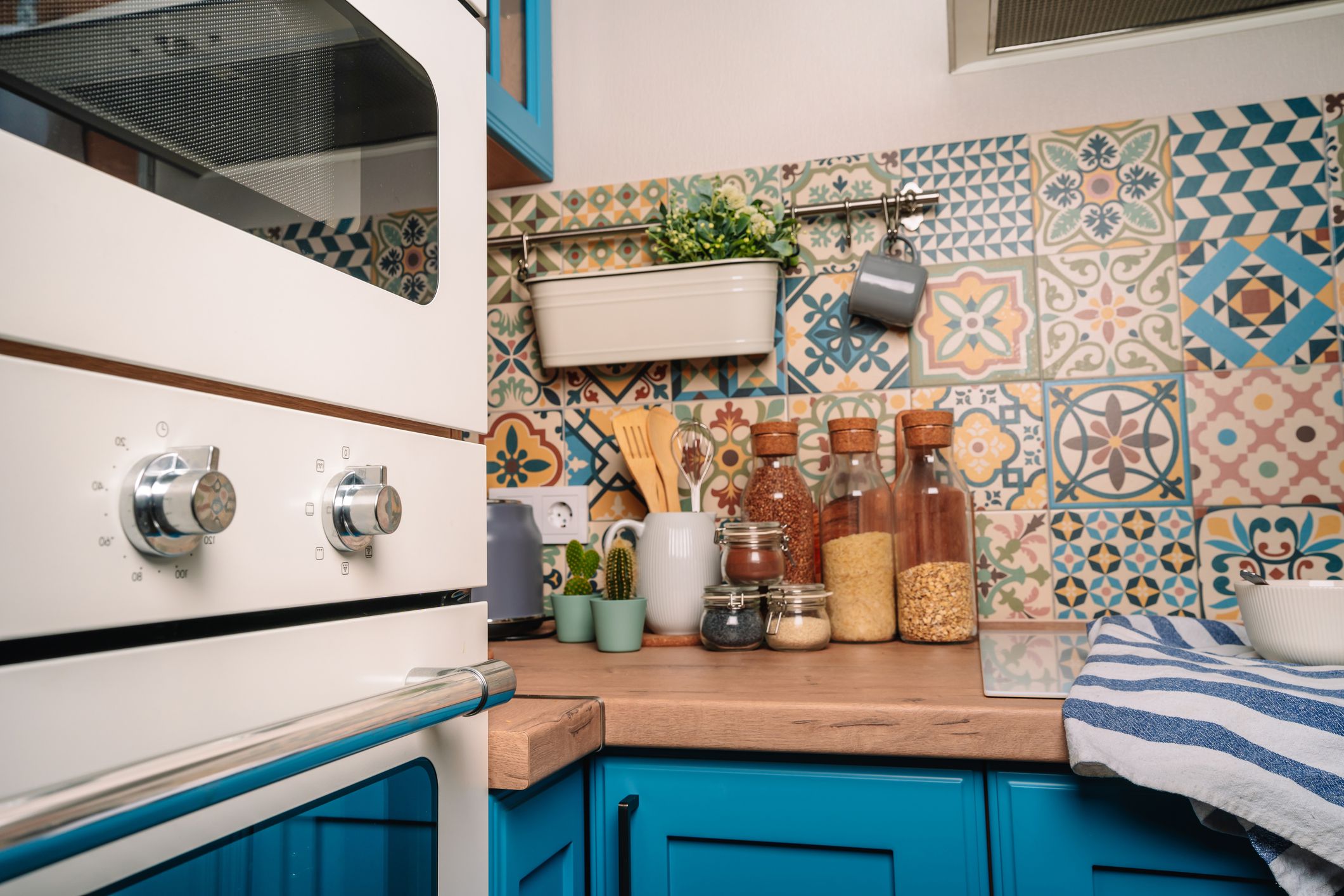 Cozy home style modern kitchen with colorful patchwork tiles, spice jars, glass jars with cereals and other kitchen accessories