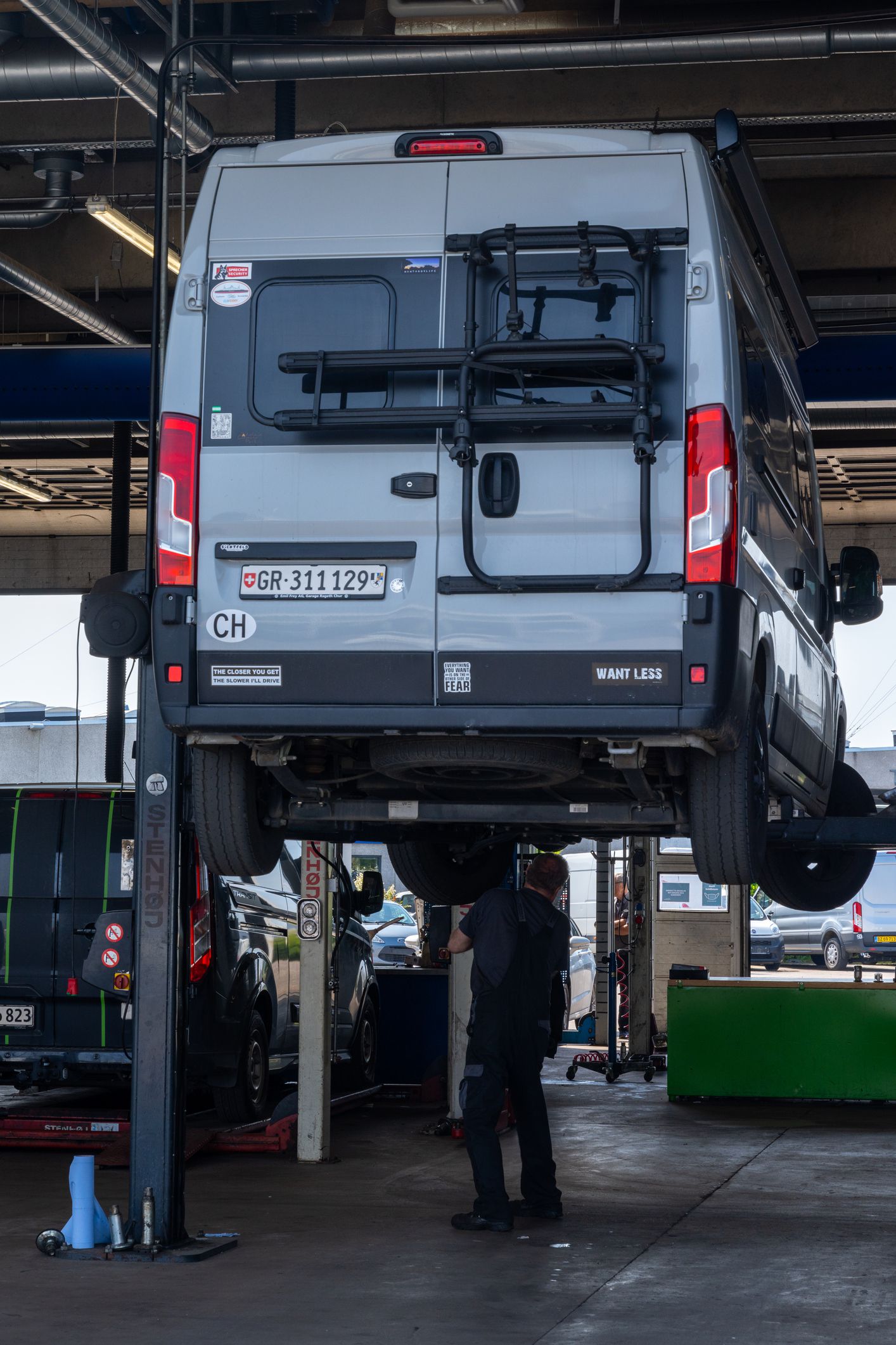 Odense, Denmark - 10 June, 2021: gray camper van in a modern garage up on the car lift with a car mechanic underneath