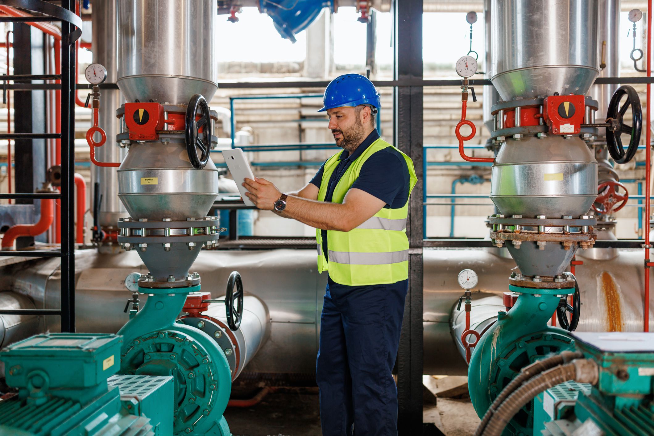 A mature Caucasian male engineer is checking the system data on his work tablet, wile standing in a heating plant.