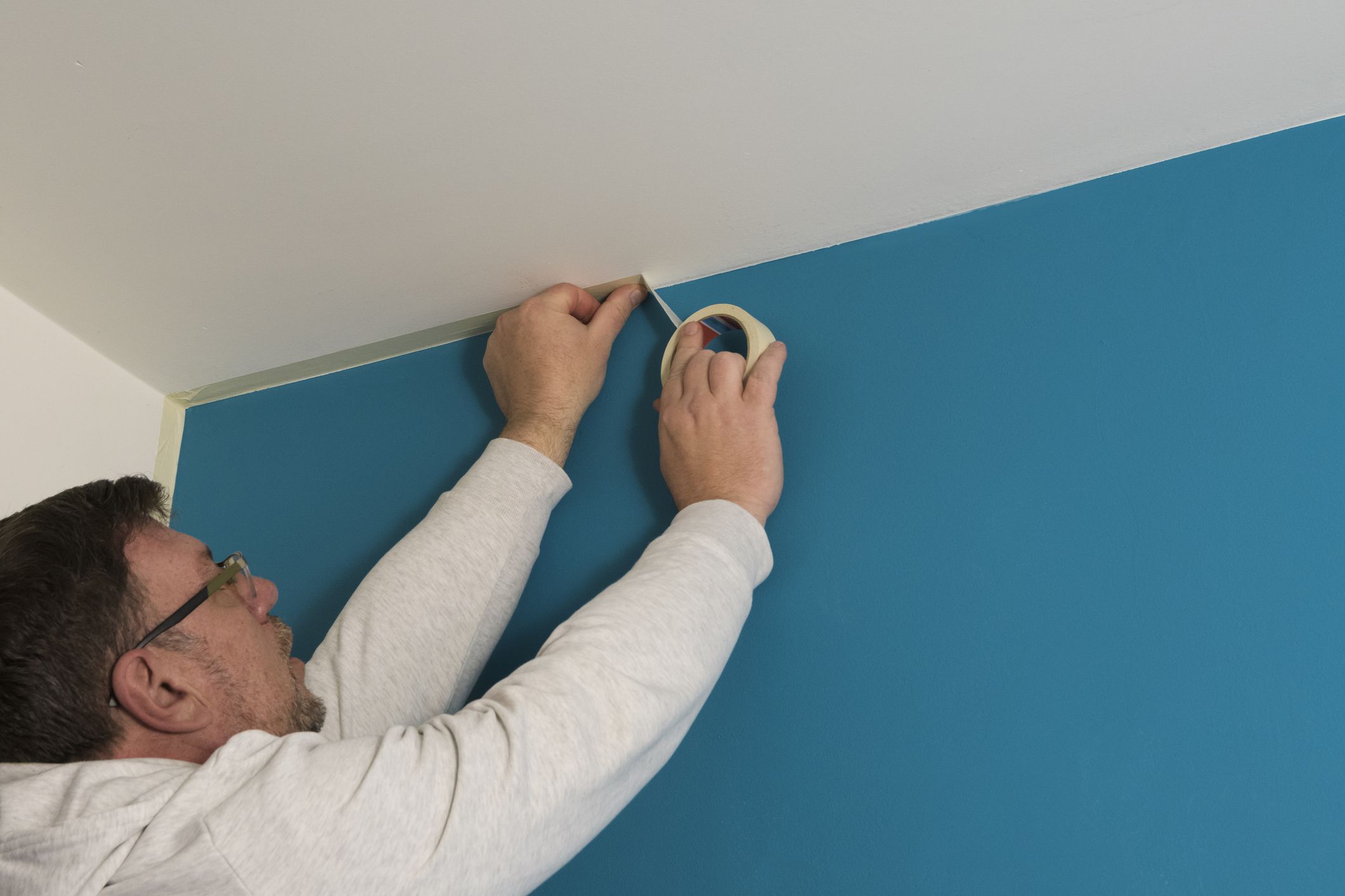 Man stick masking tape on the ceiling before painting the wall