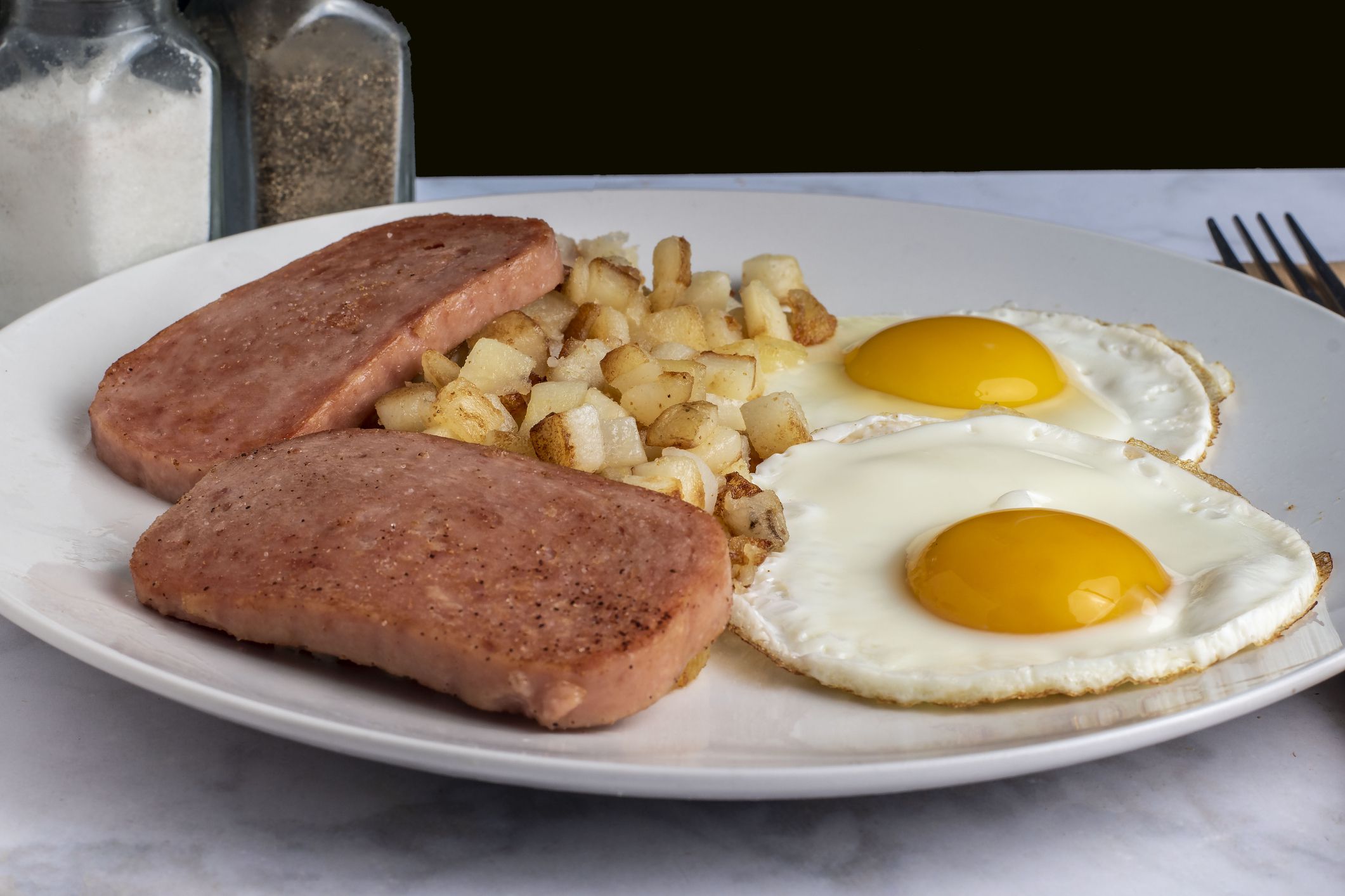 fried eggs served with fried spam and hash browns,
