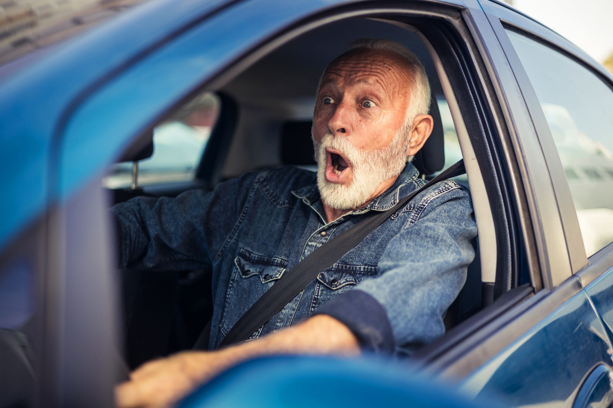 Shocked frightened man screaming and braking just before an accident. Senior man driving car is about to crash.