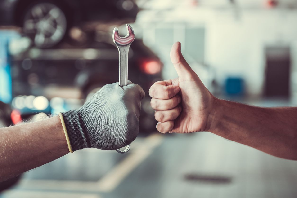 Someone holding a thumbs up while someone else holds a wrench up.