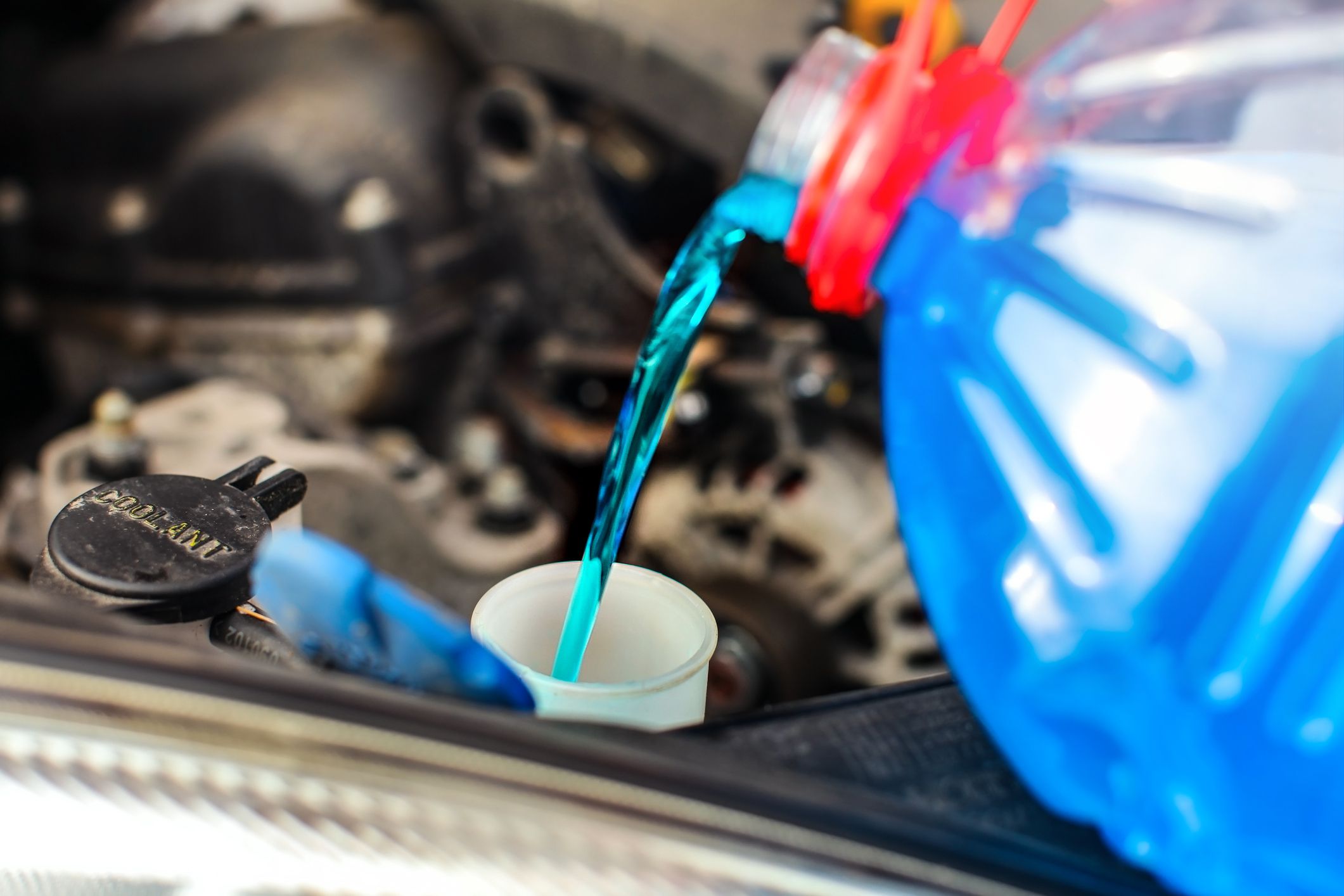 Detail on antifreeze car screen wash liquid pouring into dirty car from blue and red anti freeze water container.