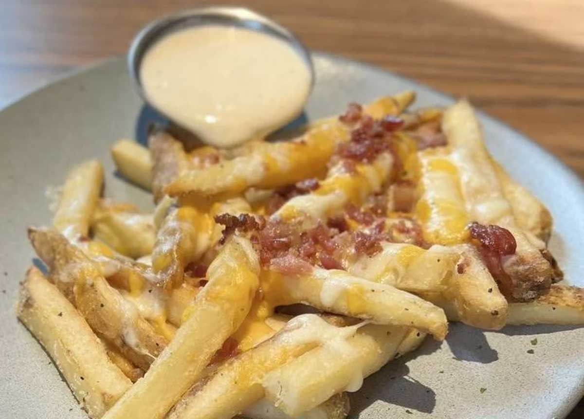 A plate of crispy beef tallow fries topped with melted cheese and savory bacon.