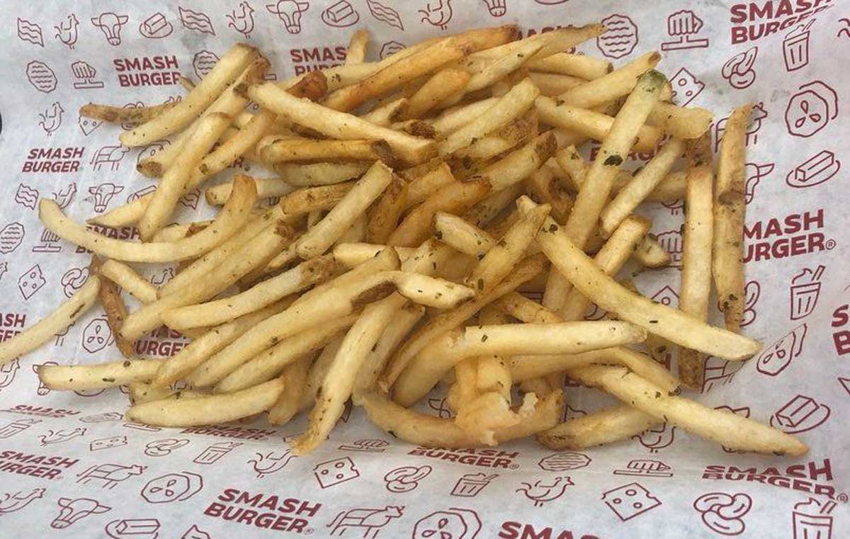 A serving of thin, seasoned beef tallow fries on Smashburger-branded paper, with the fries spread out and some seasoning visible on top.