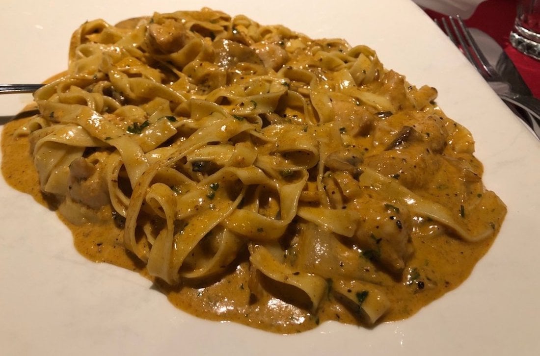 A plate of fettuccine pasta covered in a creamy, orange-brown sauce with herbs and small pieces of meat, served on a white dish.
