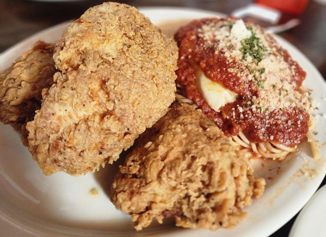 A plate with two pieces of golden-brown fried chicken and a serving of spaghetti topped with red tomato sauce, grated cheese, and herbs.