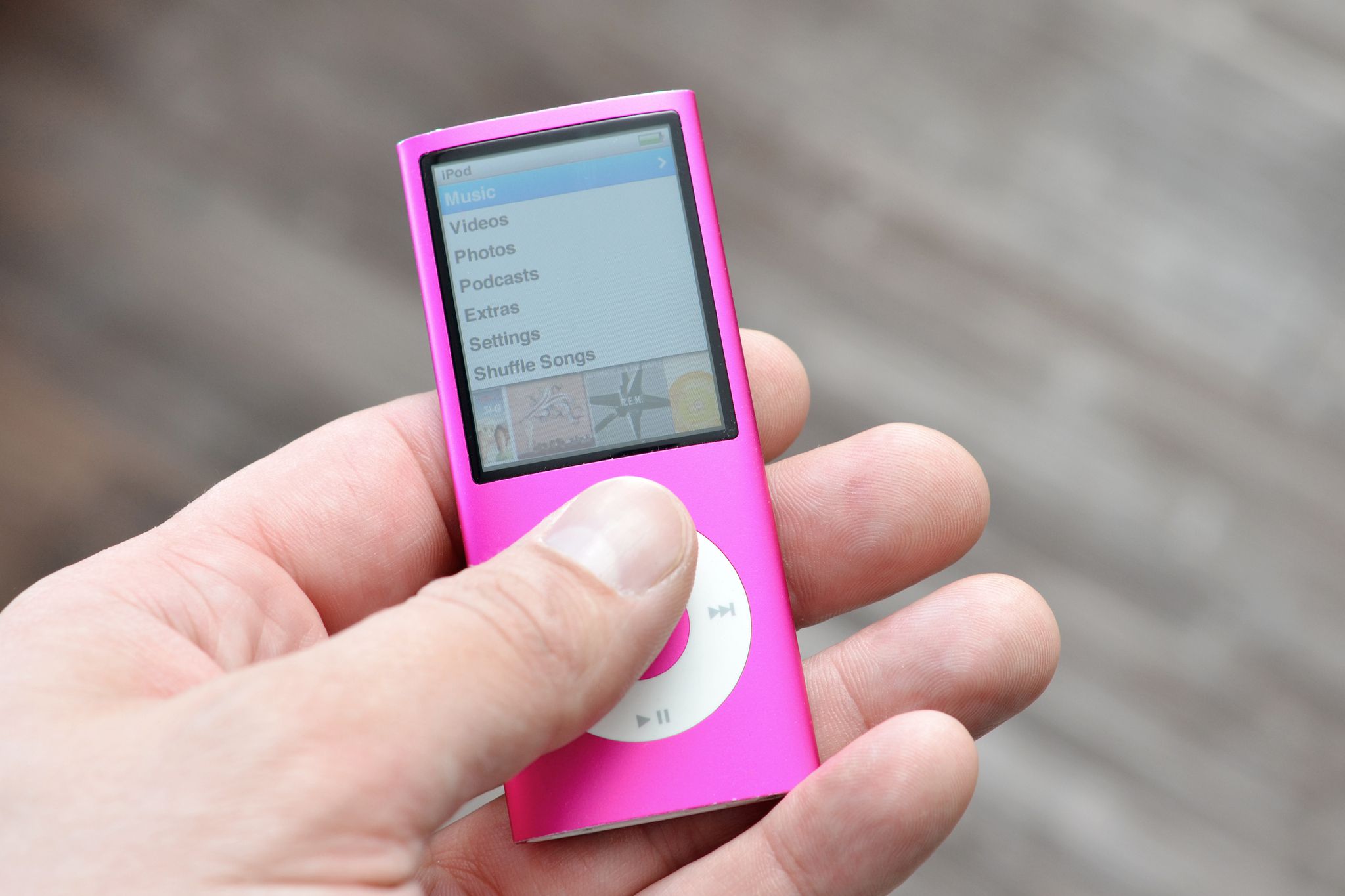 Closeup of male hand holding an old version of an iPod Nano with a blurred background of a wooden floor