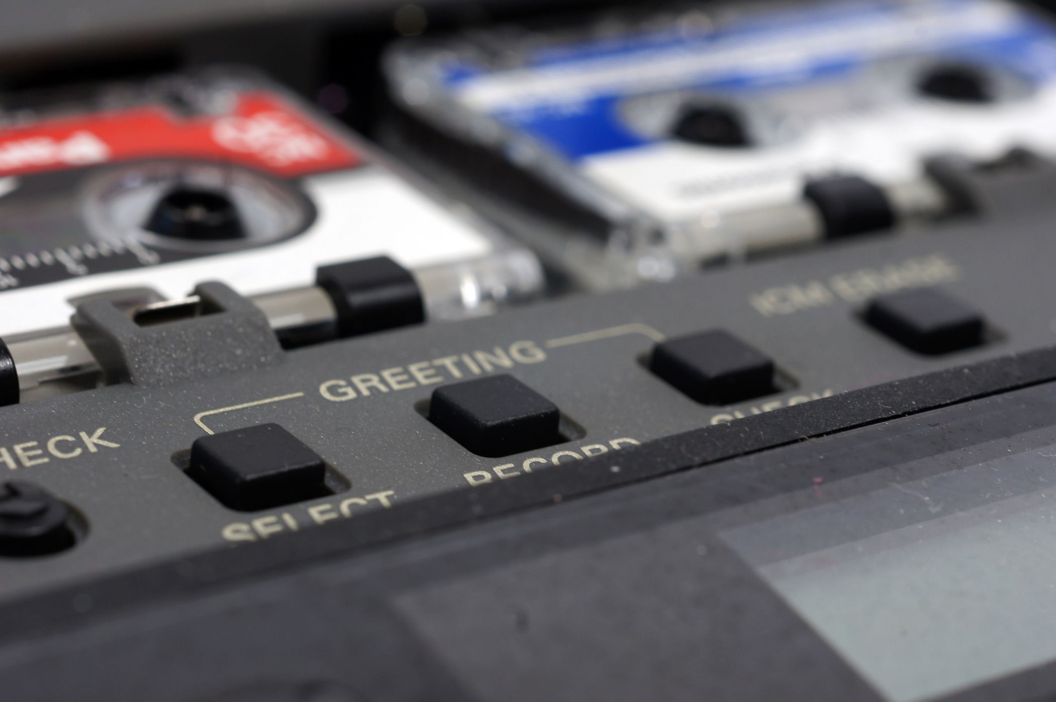 Closeup of two mini cassette tapes in an old answering machine with greeting setting buttons among other buttons