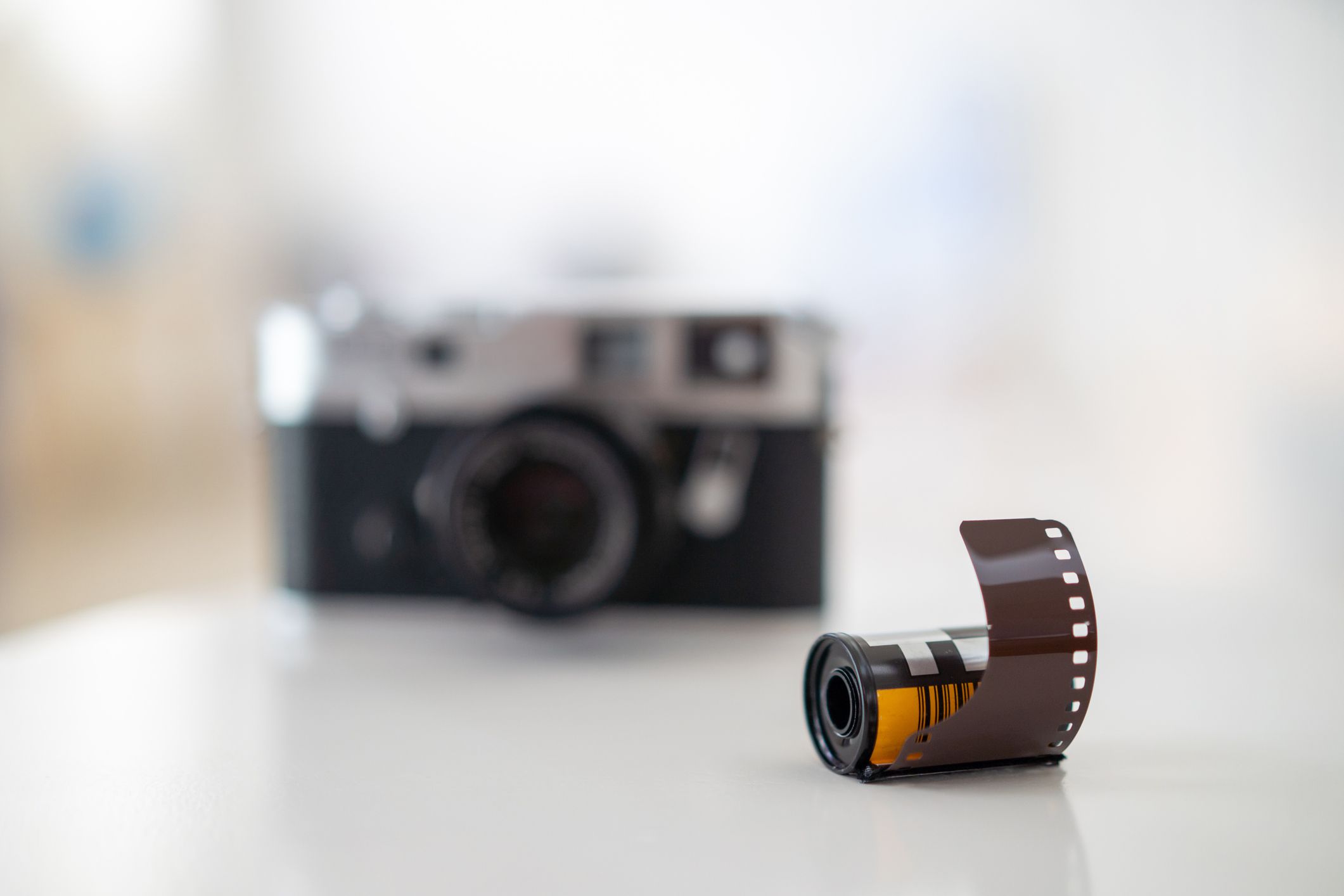 Closeup of a roll of 35mm film on a white table with a blurred background of a vintage analog camera