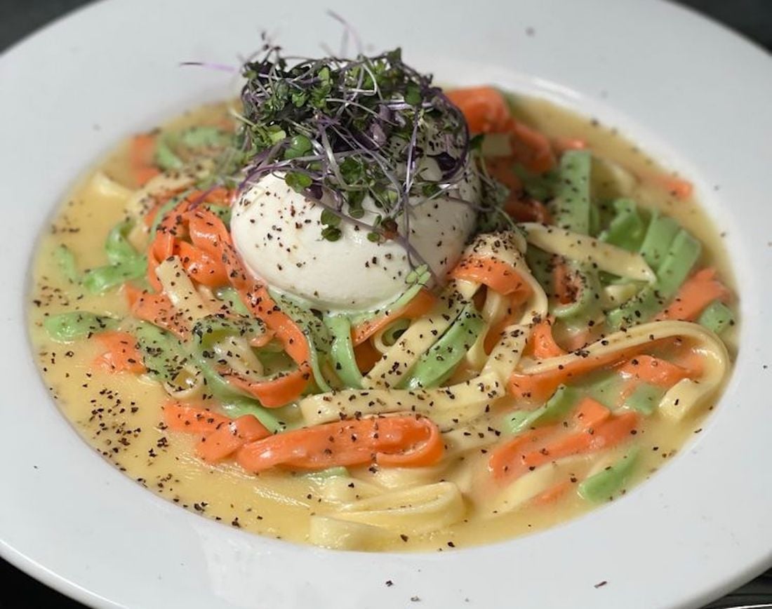 A plate of creamy tri-color fettuccine pasta topped with a ball of burrata cheese, sprinkled with black pepper and garnished with microgreens.