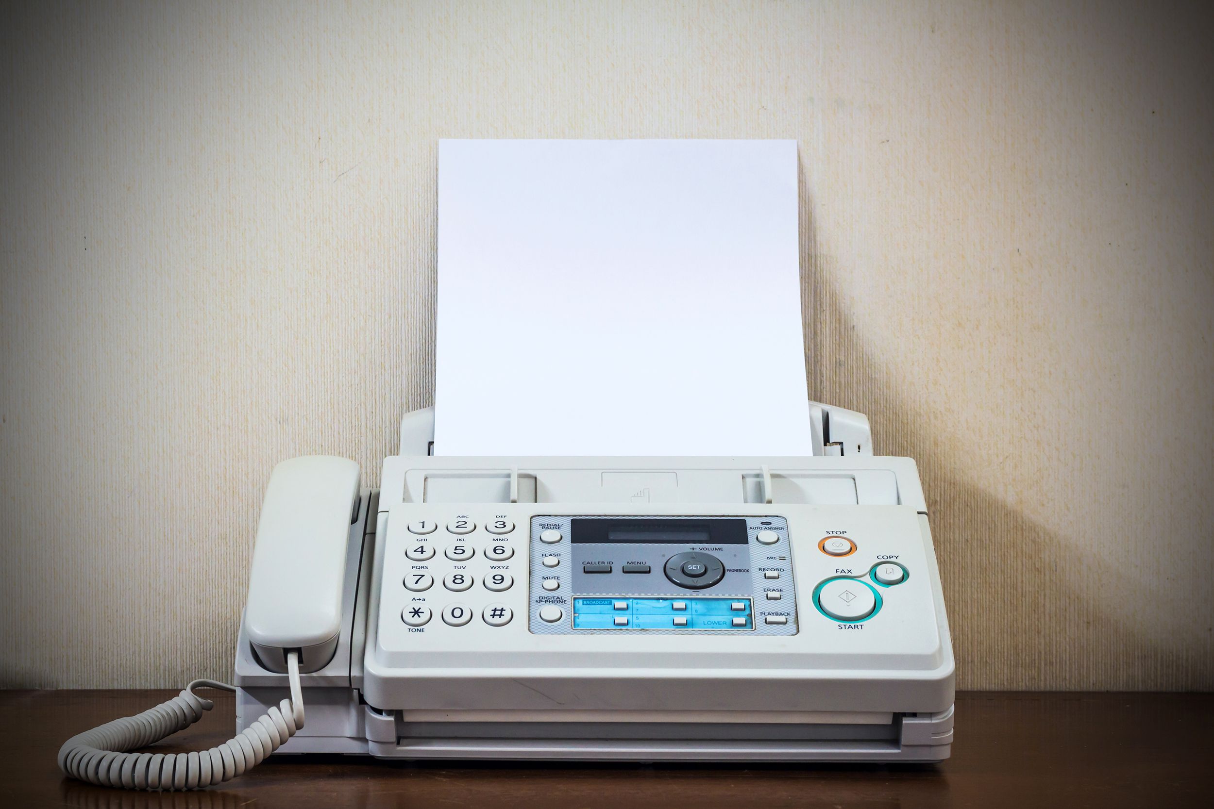 Vintage fax machine with sheets of white paper and phone on a wooden desk, against a white wall, vintage look