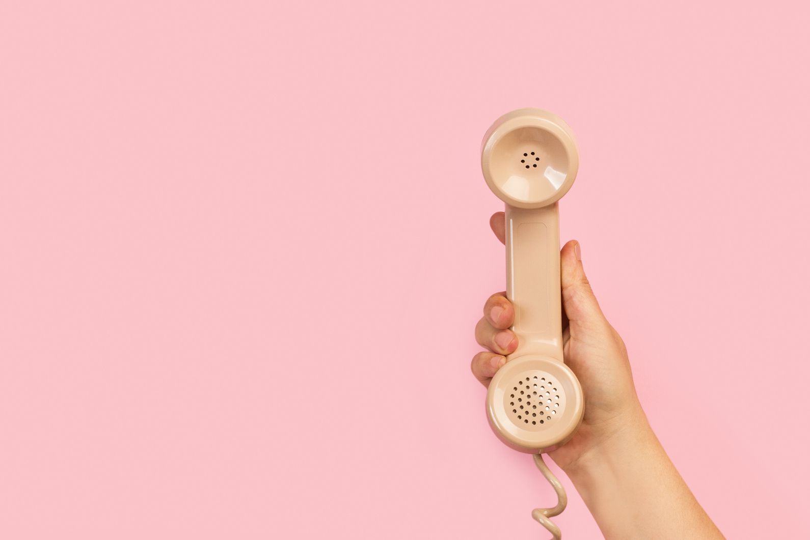 Female hand holding beige telephone receiver on a pink background