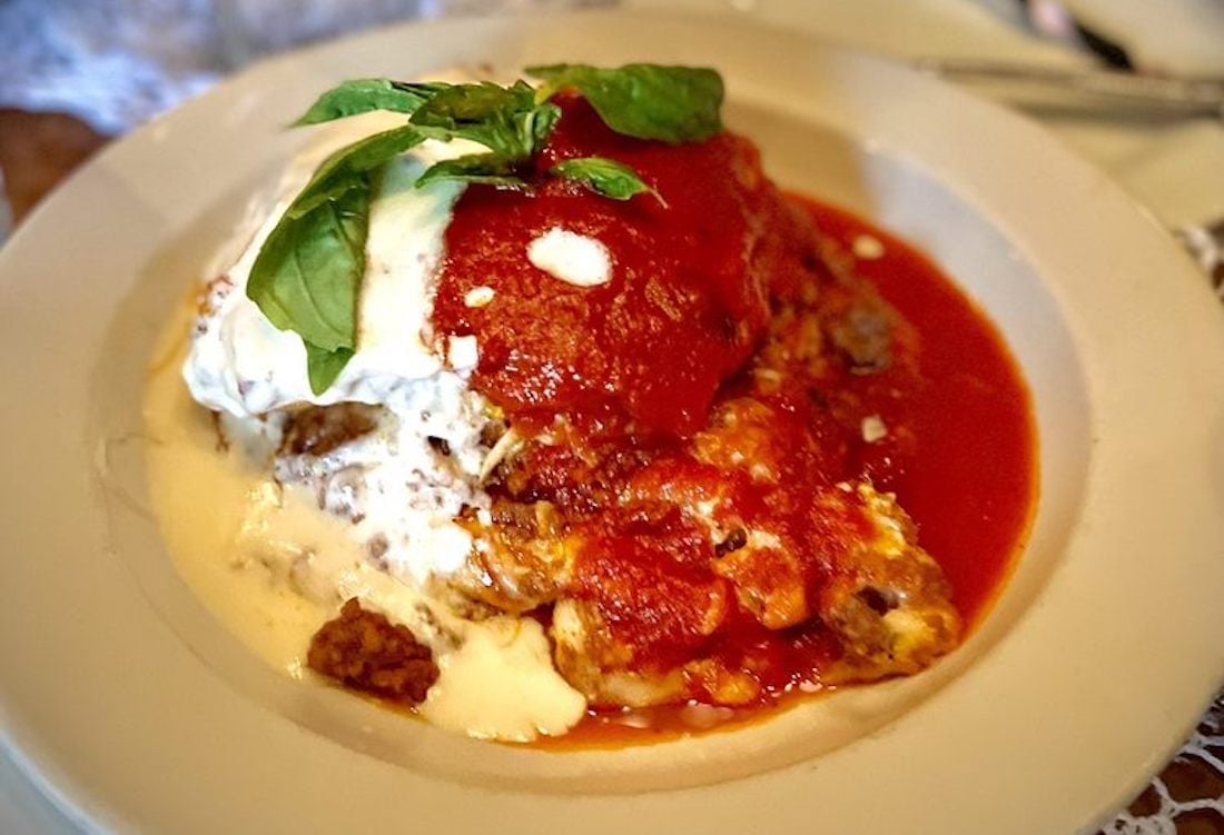 A plate of lasagna topped with tomato sauce, melted cheese, and fresh basil leaves, served with extra sauce on a white dish.