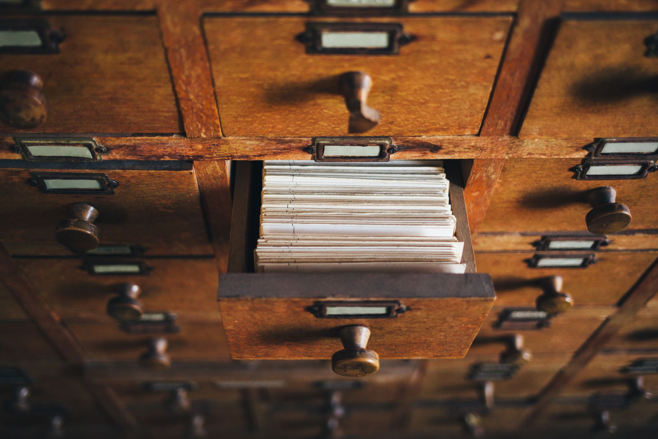 Focus on one open drawer with numerous white index cards in an old wooden card catalog