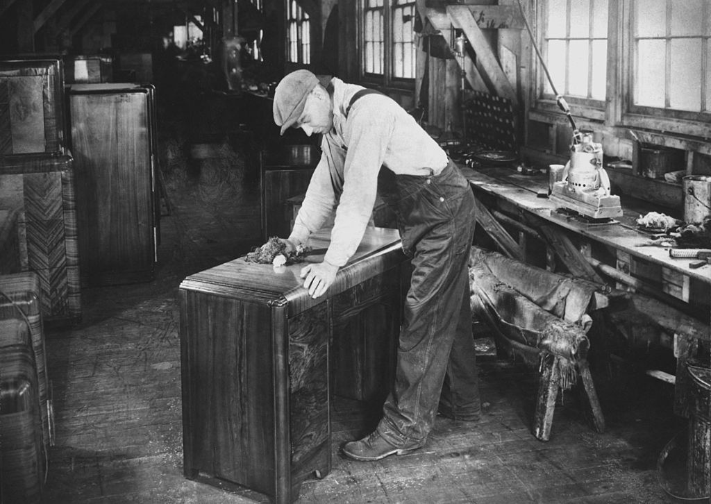 A factory worker polishes the top of a desk in a furniture factory, USA, circa 1950