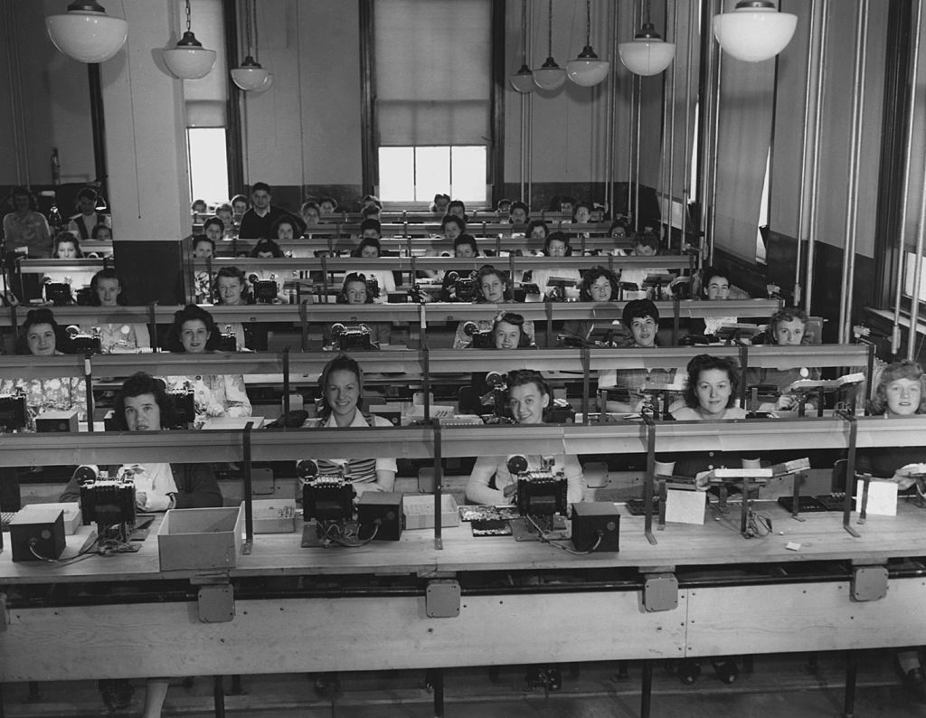 Female workers sit in rows behind a workspace on an assembly line in a factory, USA, circa 1950.