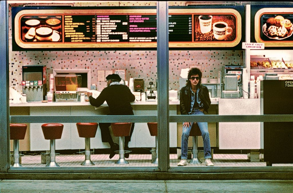 Portrait of American Rock musician Earl Slick as he sits at the counter of a Dunkin' Donuts storefront, Washington DC, 1982.