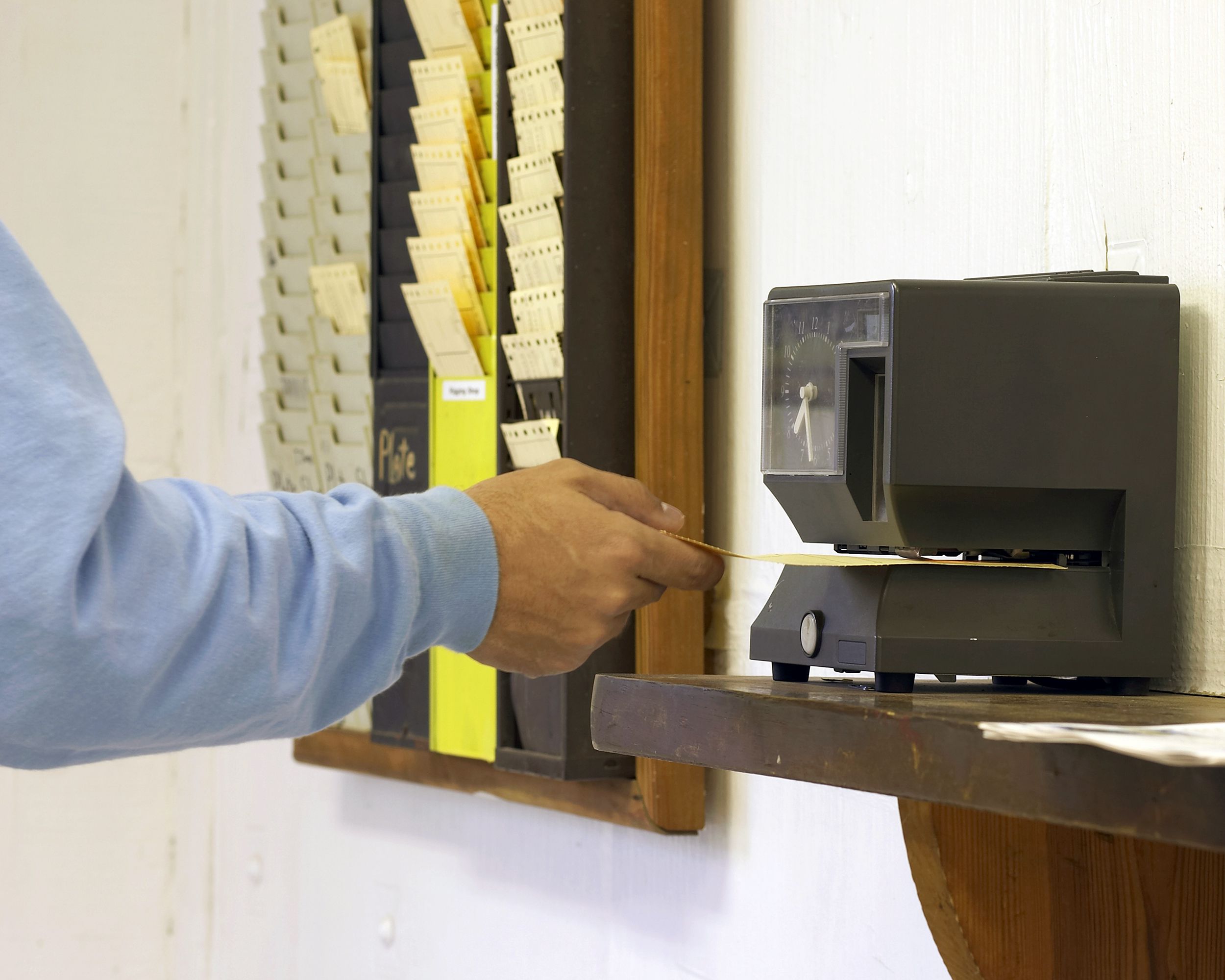 Male worker punching punch card with four rolls of other workers' cards on the wall
