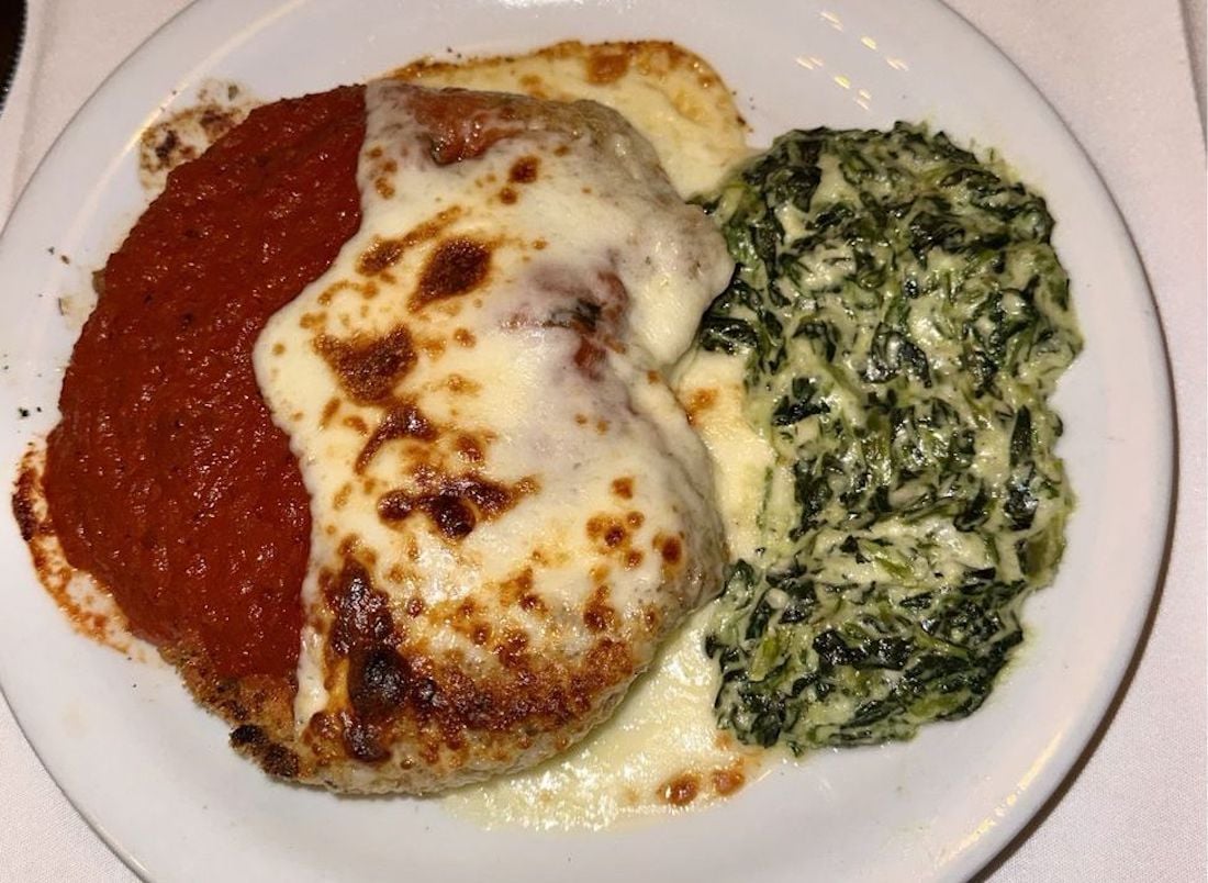 A plate with chicken parmesan topped with tomato sauce and melted cheese, served next to a creamy spinach side dish.