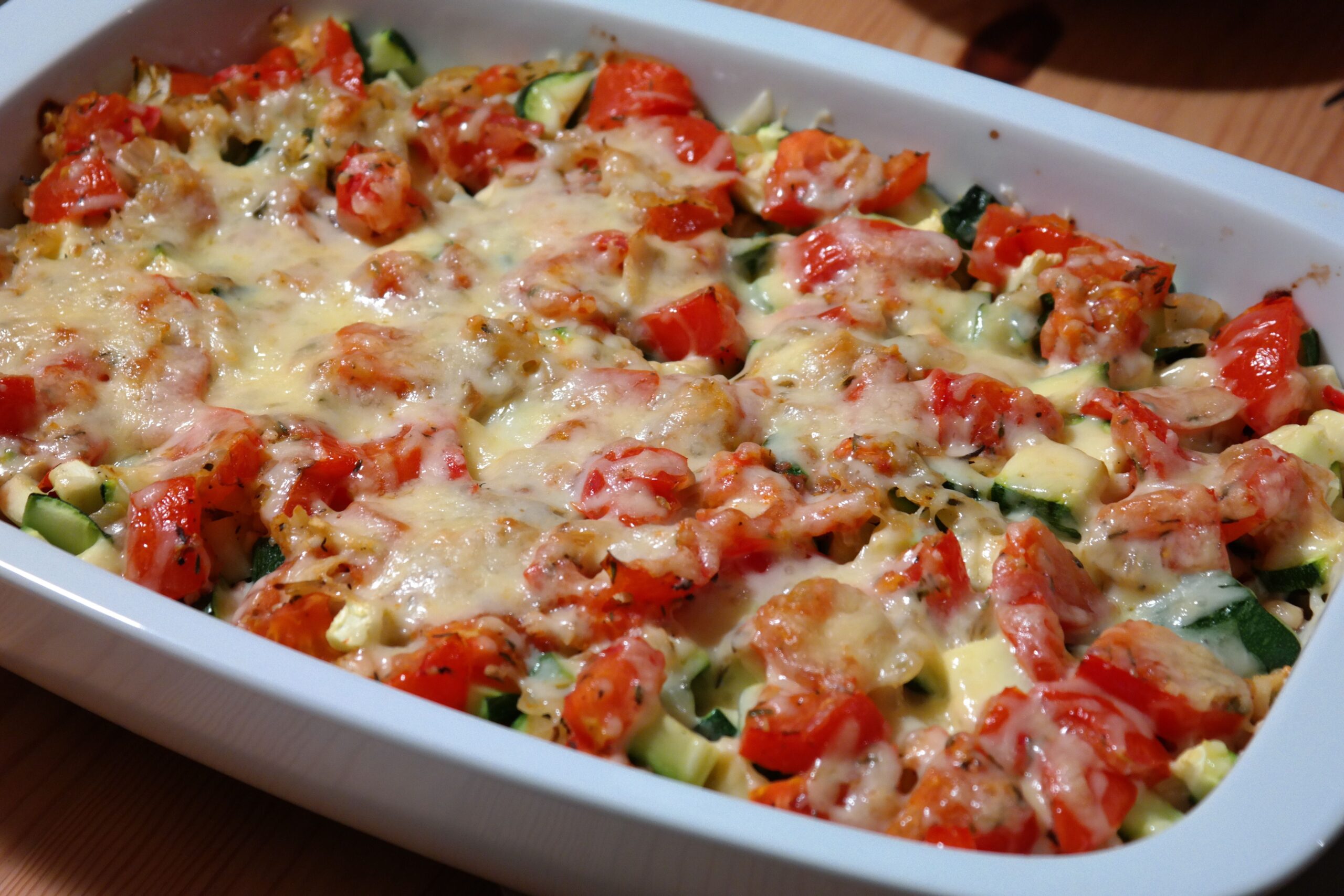 Casserole in a white rectangular baking dish with broccoli, tomatoes, courgettes and cheese.